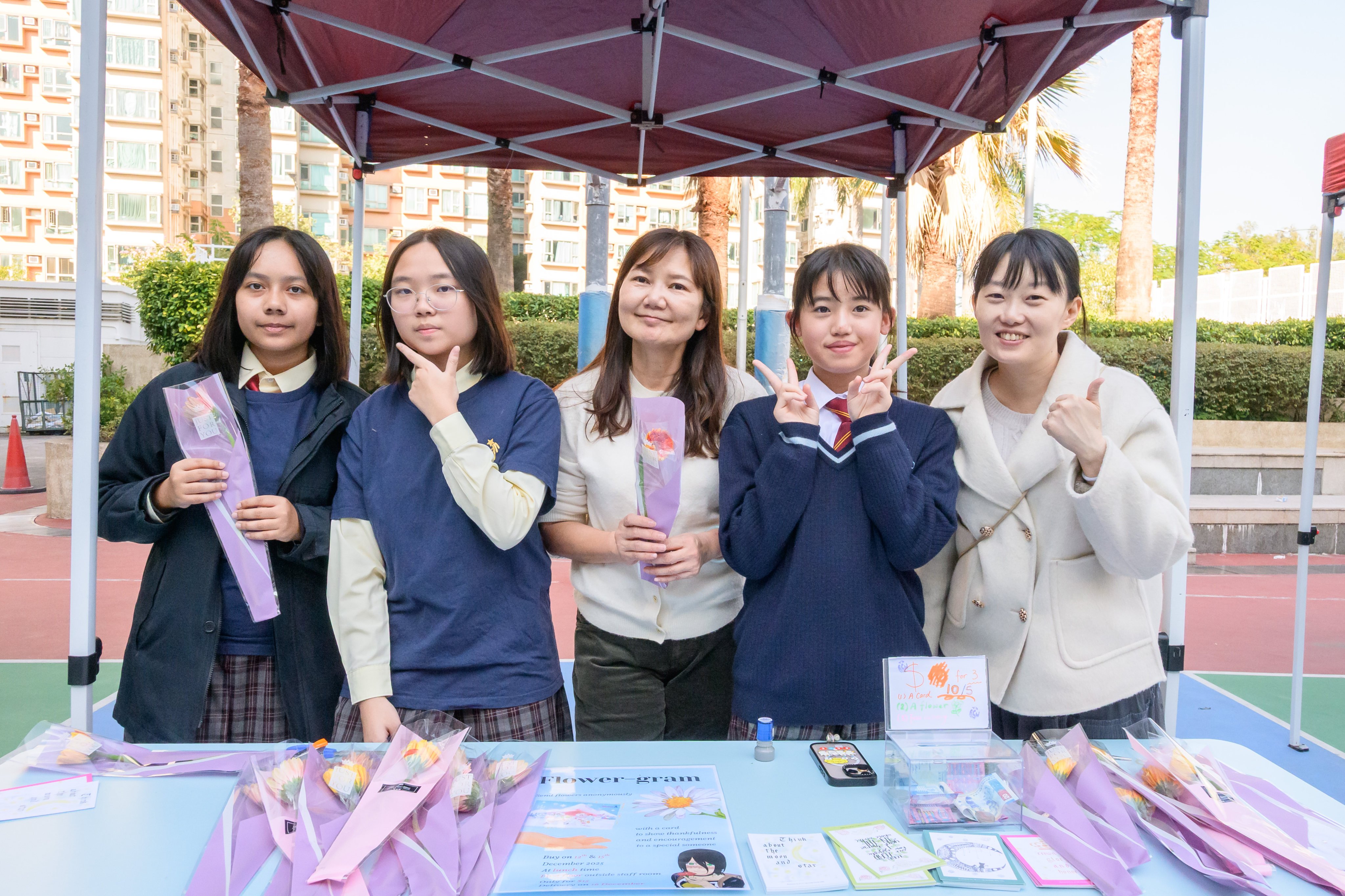 Students Allie Poon Wai-yan (far left) and Hebe Lee Pui-hei (second left) sell flowers and charity postcards distributed by Hong Kong Disneyland to raise money for Operation Santa Claus during the school funfair. Photo: Handout