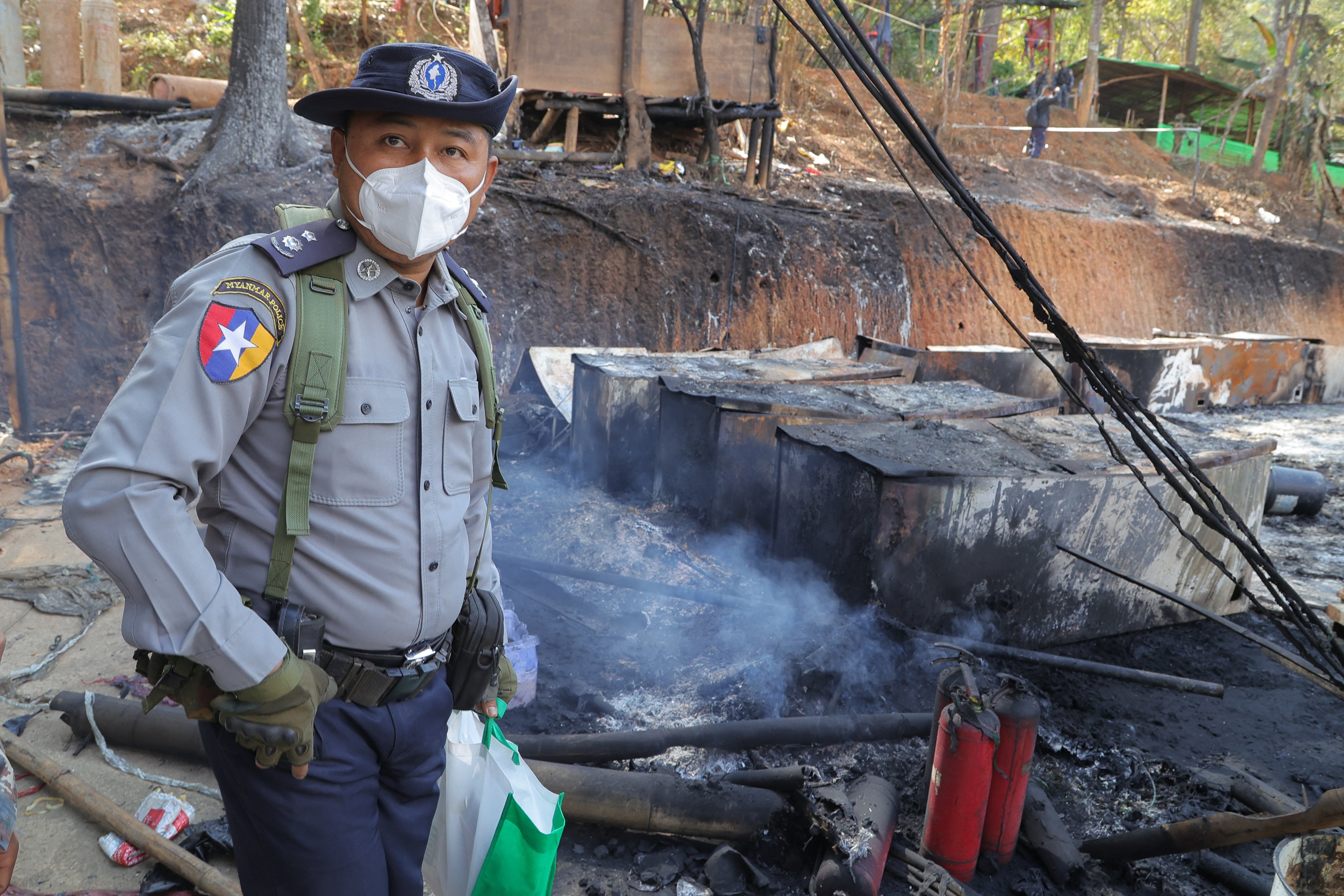 A Myanmar police officer stands in the smoldering ruins of a captured methamphetamine lab near Namlan in Shan State on January 14, 2026. (Photo by Joe STENSON / AFP)
