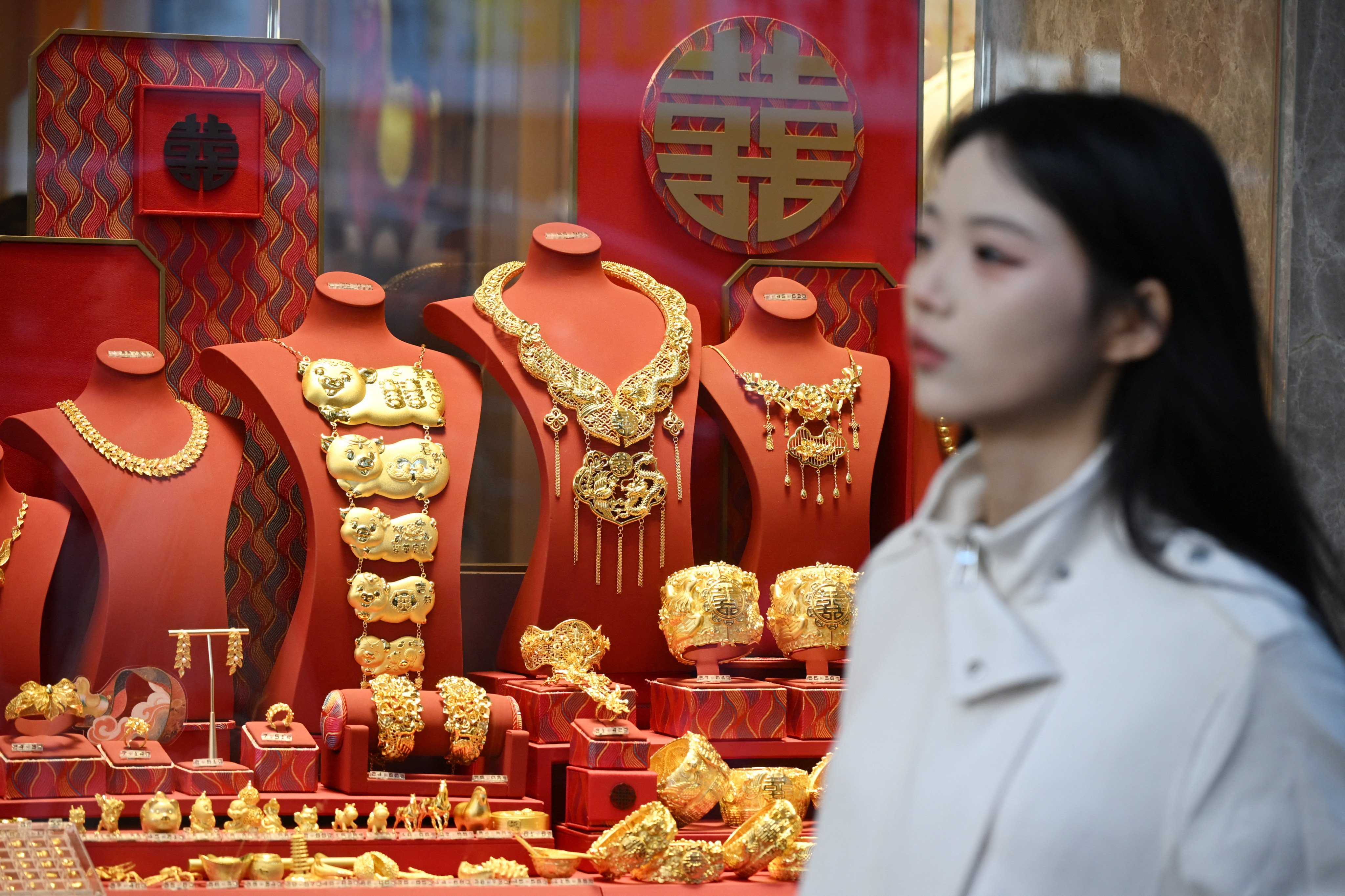 A woman walks past a shop selling gold in Hong Kong on January 26, 2026. The price of safe-haven asset gold surpassed 5,000 USD, hitting a record amid rising global uncertainty and turmoil set off by US President Donald Trump’s policies. (Photo by Peter PARKS / AFP)