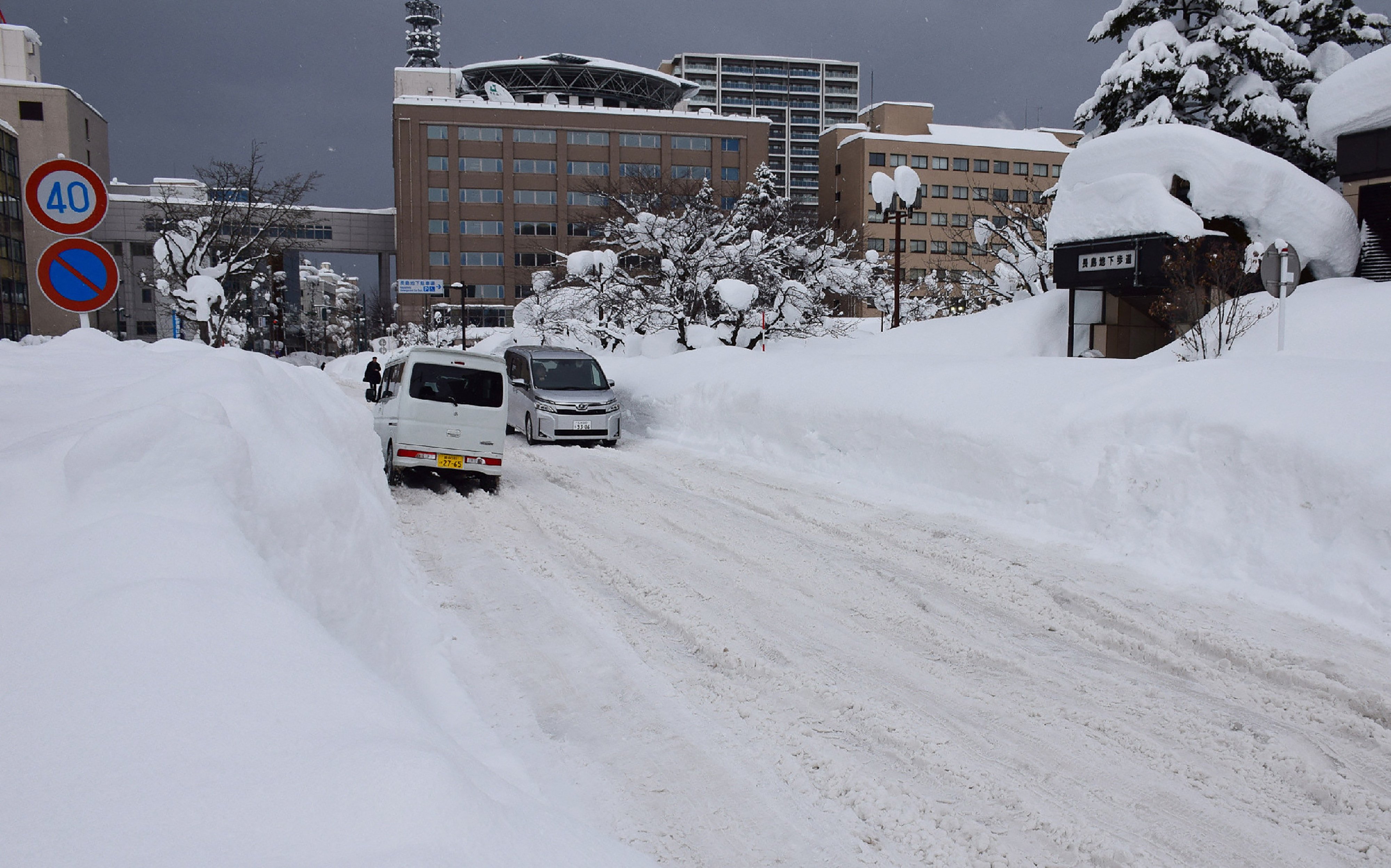 People commute along a snow-covered street in Aomori City on February 3, 2026. Unusually heavy snow in Japan has been blamed for 30 deaths in the past two weeks, officials said on February 3, including a 91-year-old woman found under a three-metre pile outside her home. (Photo by JIJI Press / AFP) / Japan OUT / JAPAN OUT
