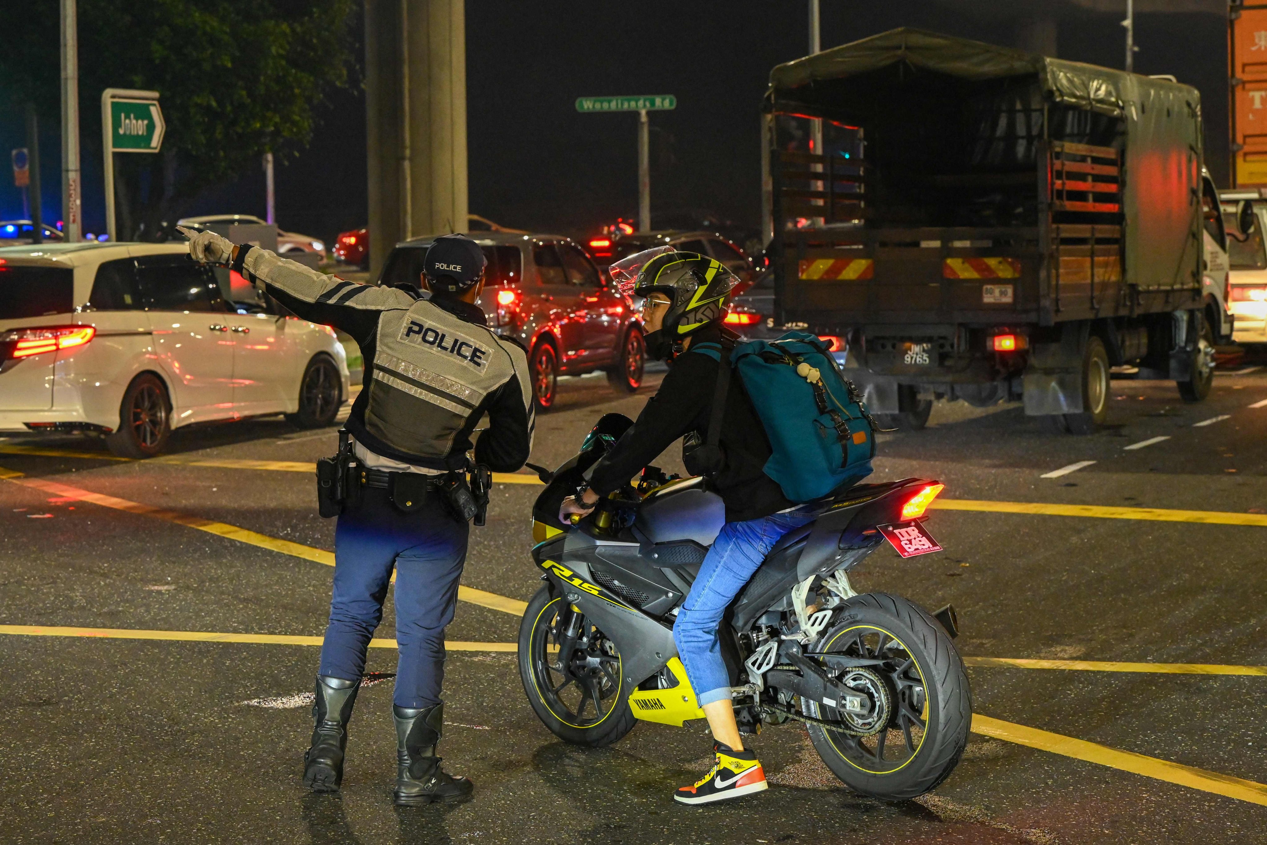 A traffic police officer guides a motorcyclist as vehicles queue to enter the Woodlands Checkpoint in Singapore. Photo: AFP