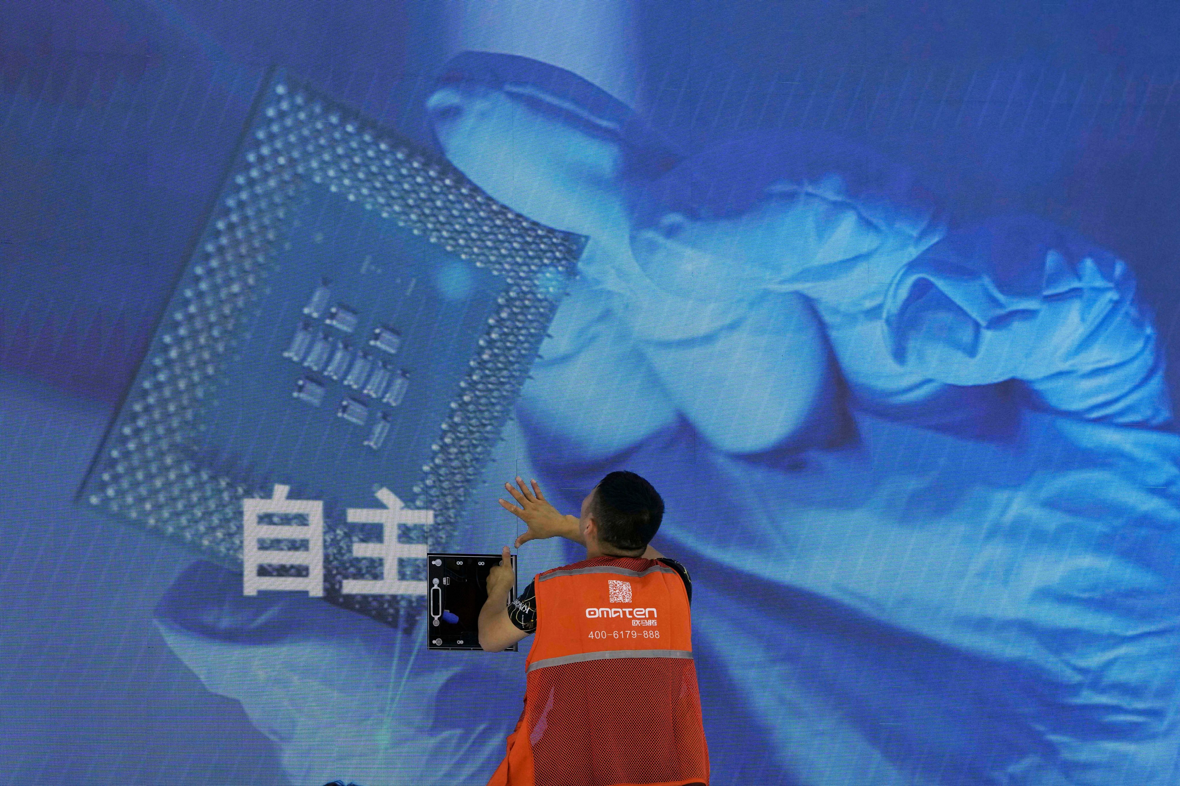 A worker adjusts a  display panel showing a computer chip and the Chinese characters for “independence” at the Sugon booth during the World AI Conference in Shanghai, July 5, 2023. Photo: AP