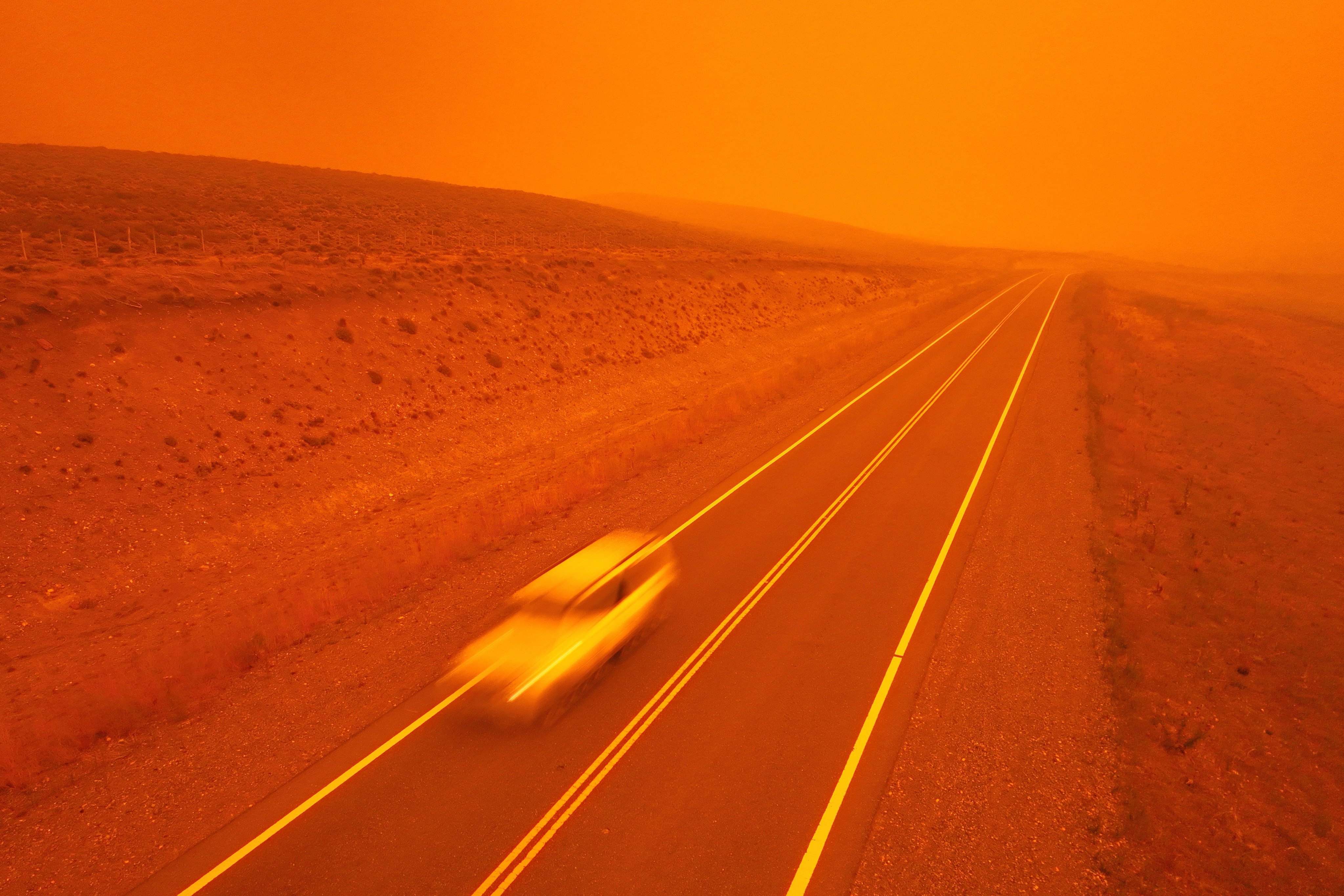 A car speeds along a road as smoke from wildfires turns the sky red near Cholila, Argentina. Photo: AP