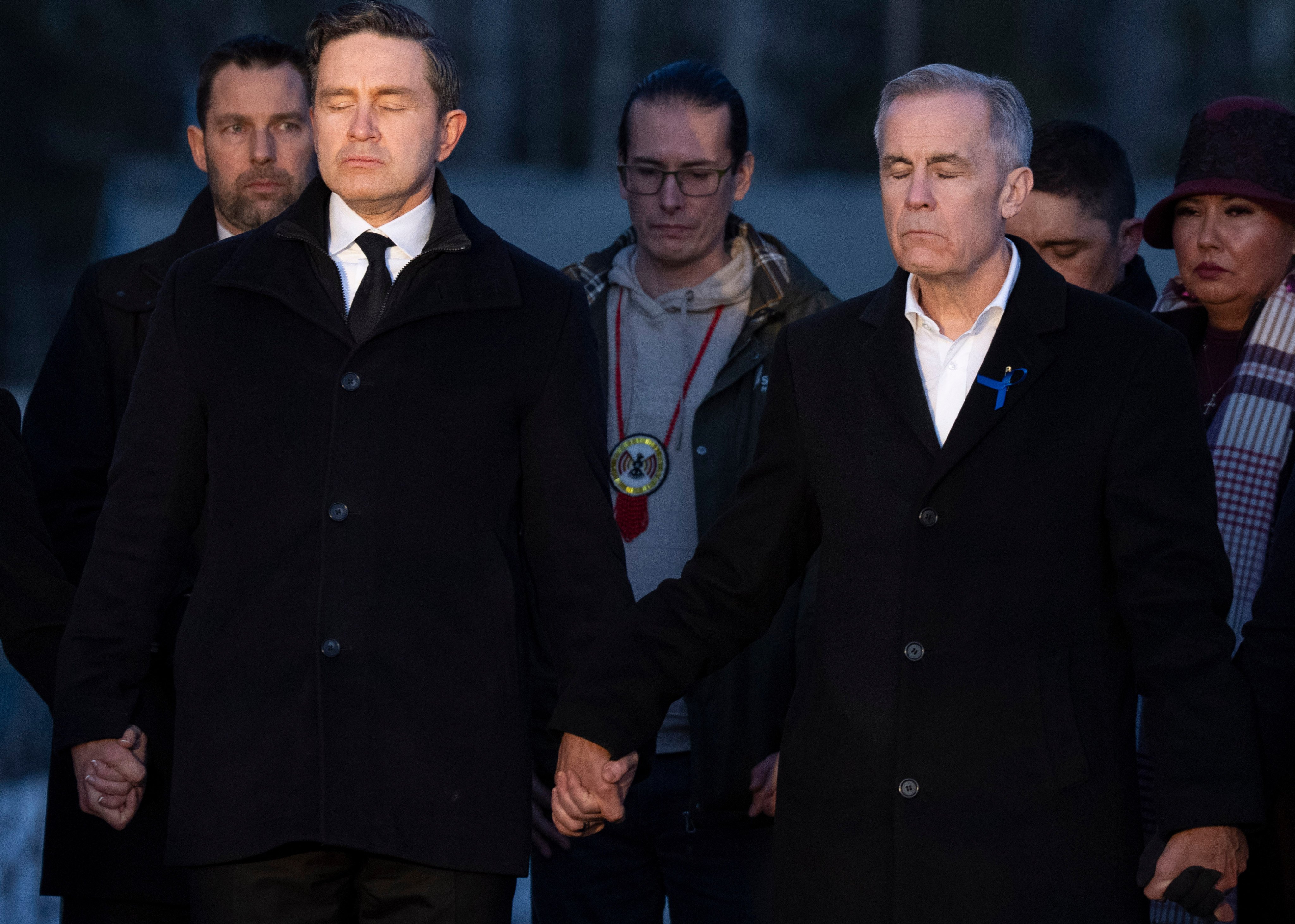 Prime Minister Mark Carney, right, and Conservative Leader Pierre Poilievre join hands while attending a vigil for the victims of a mass shooting, in Tumbler Ridge, BC, on Friday. Photo: AP