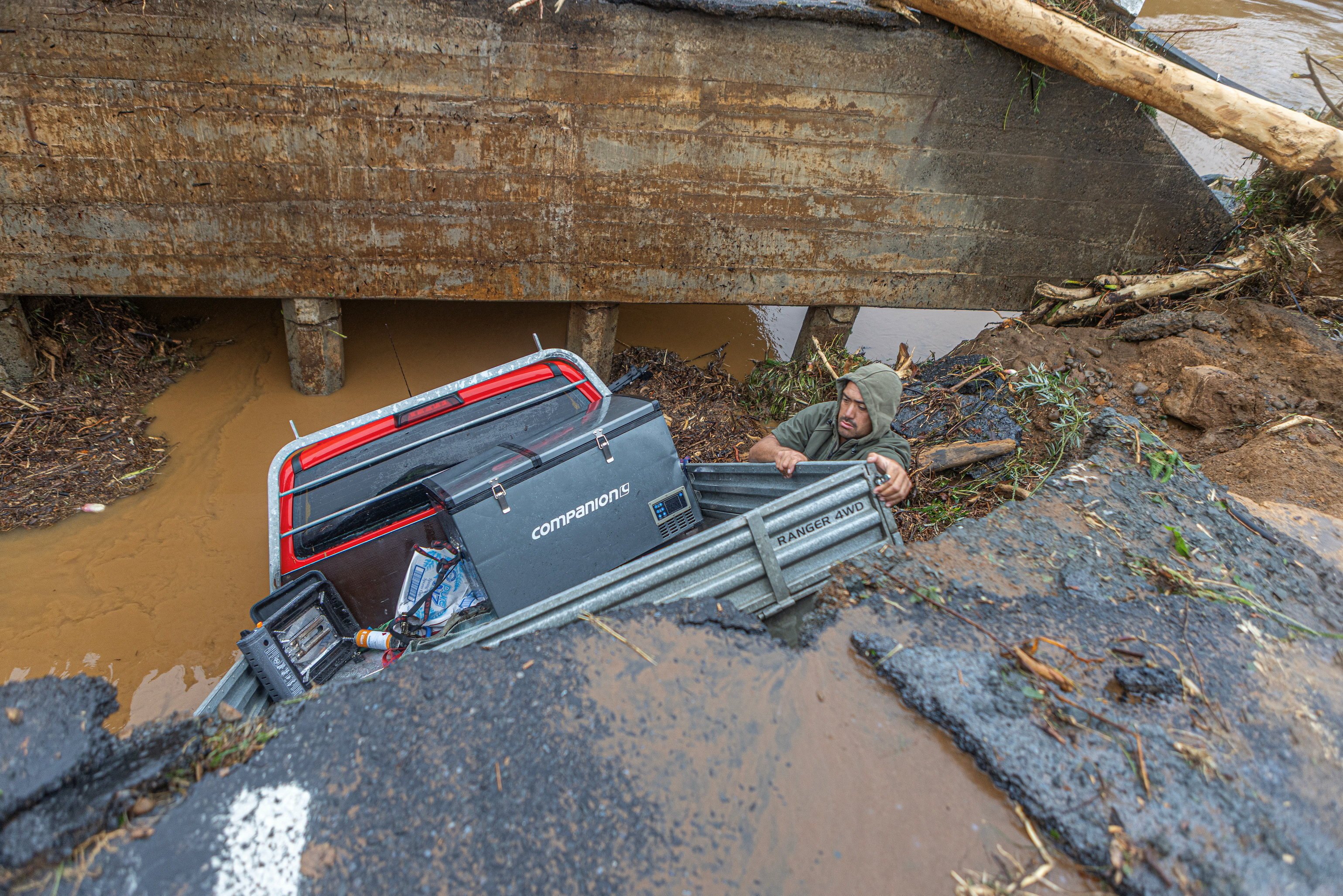 A man retrieves his belongings from a utility vehicle that plunged off a collapsed section of road in Puketotara, New Zealand, on Saturday. Photo: Wayne Feisst via Reuters