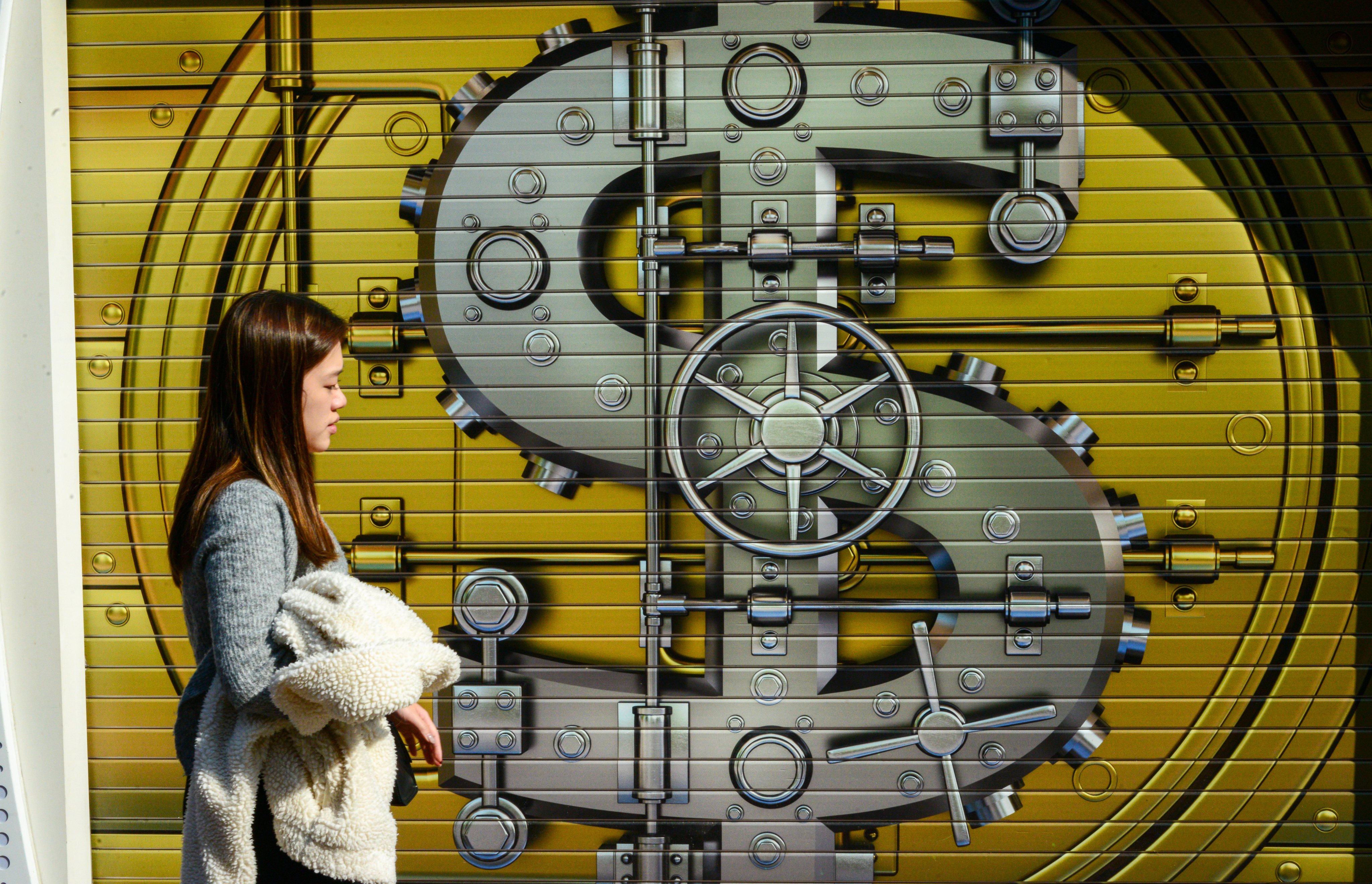 A pedestrian passes in front of a currency mural on a shop’s gate in Hong Kong. Photo: Antony Dickson