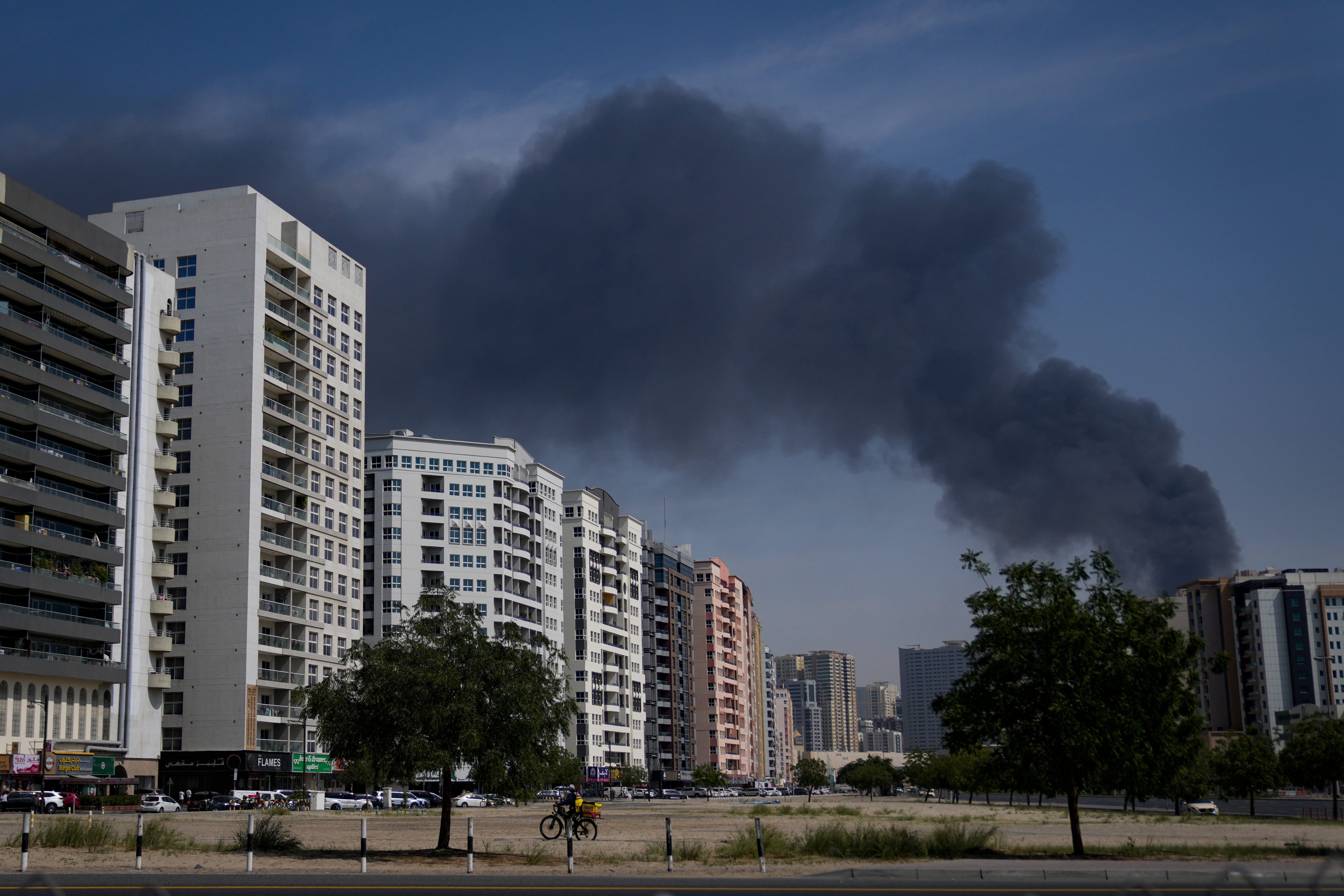 A cyclist rides past as a black plume of smoke is seen rising from a warehouse in the industrial area of Sharjah City in the United Arab Emirates following reports of Iranian strikes in Dubai, United Arab Emirates on March 1, 2026. Photo: AP