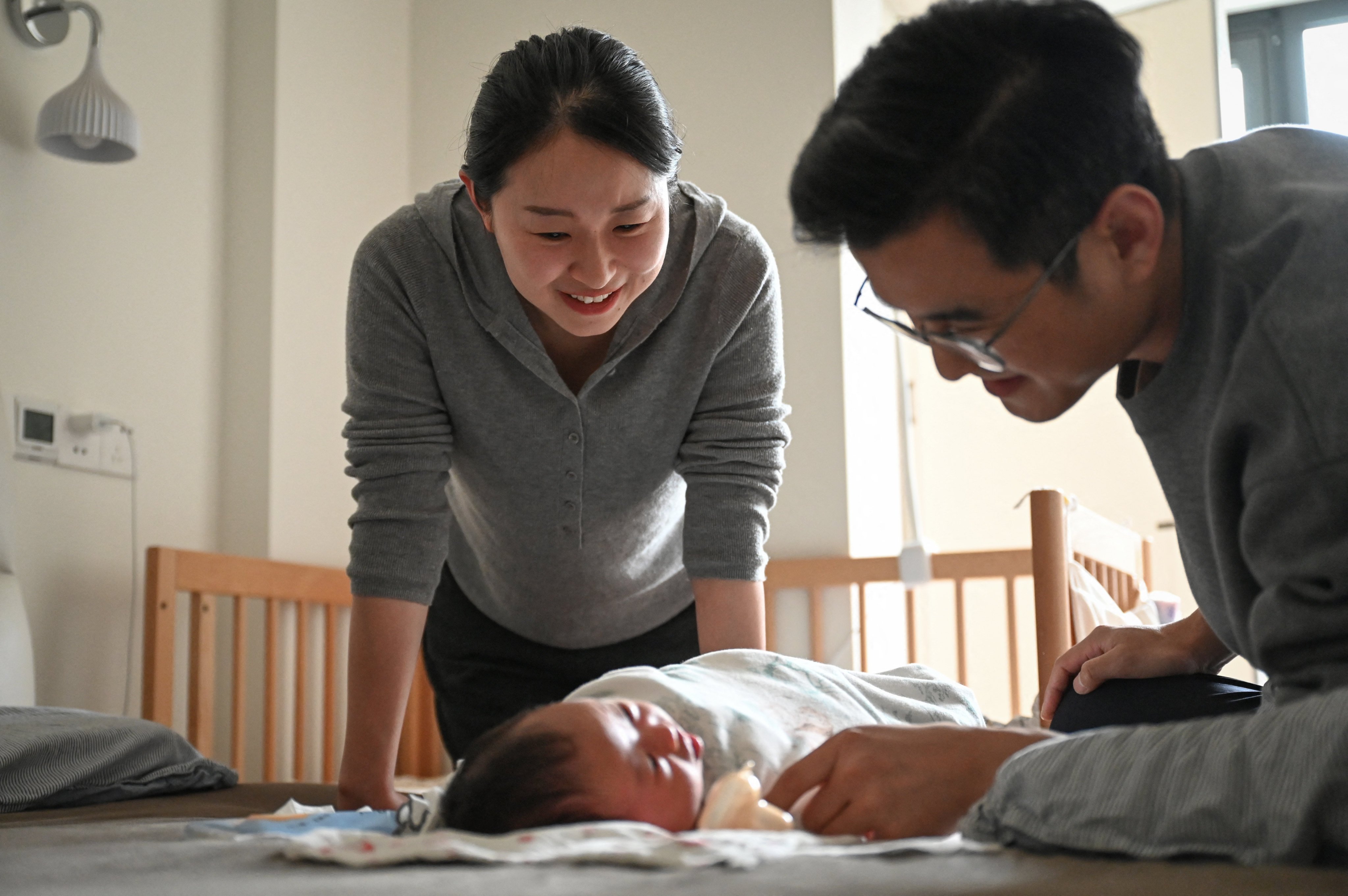 The photo taken on February 9, 2026 shows Wang Yifan (L) and her husband taking care of their new-born baby at their home in Shanghai. Renowned obstetrician Duan Tao created a digital double for healthcare app AQ, which now boasts more than 100 million users in a display of how high-tech parts of China’s medical sector have become. (Photo by Jade GAO / AFP) / TO GO WITH SOTRY: CHINA-ECONOMY-POLITICS-HEALTH-TECH-AI, FOCUS BY REBECCA BAILEY