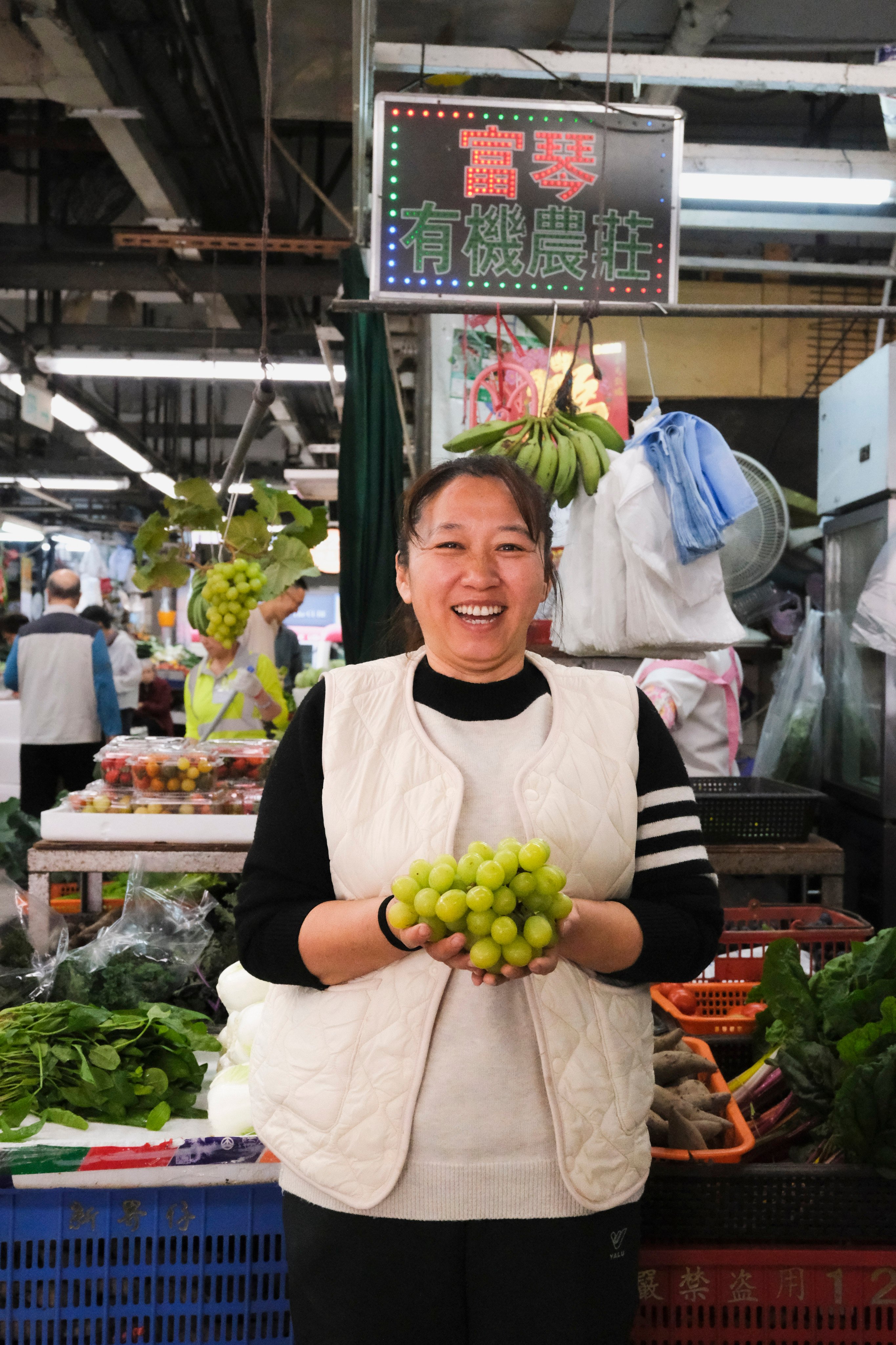 Organic farmer Yan Fuqin holds a bunch of her farm’s shine muscat grapes at her stall at Hong Kong’s Tsuen Wan Market. Photo: Hei Kiu Au