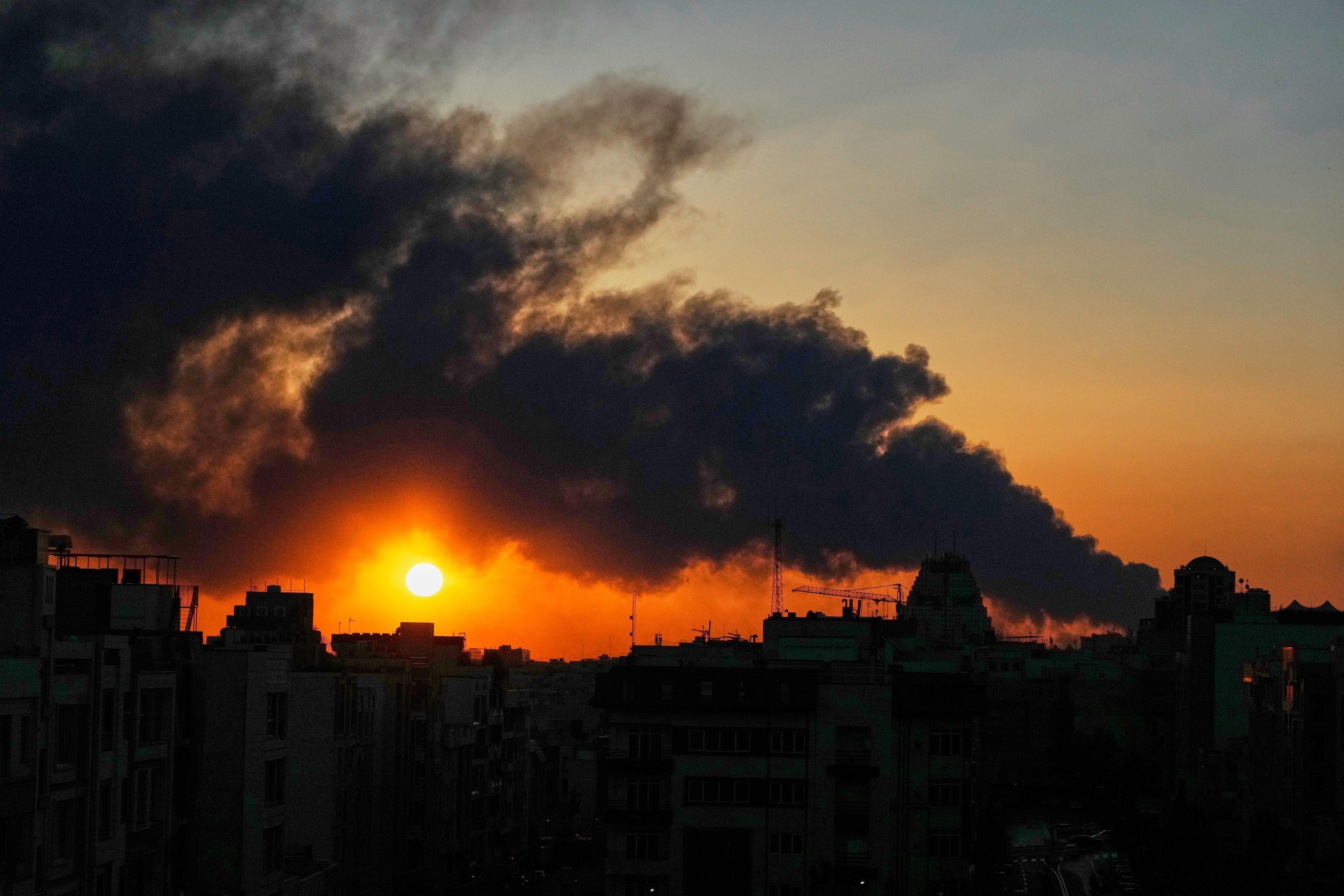 The sun sets behind a plume of smoke from a US–Israeli military strike in Tehran, Iran, on Tuesday. Photo: AP