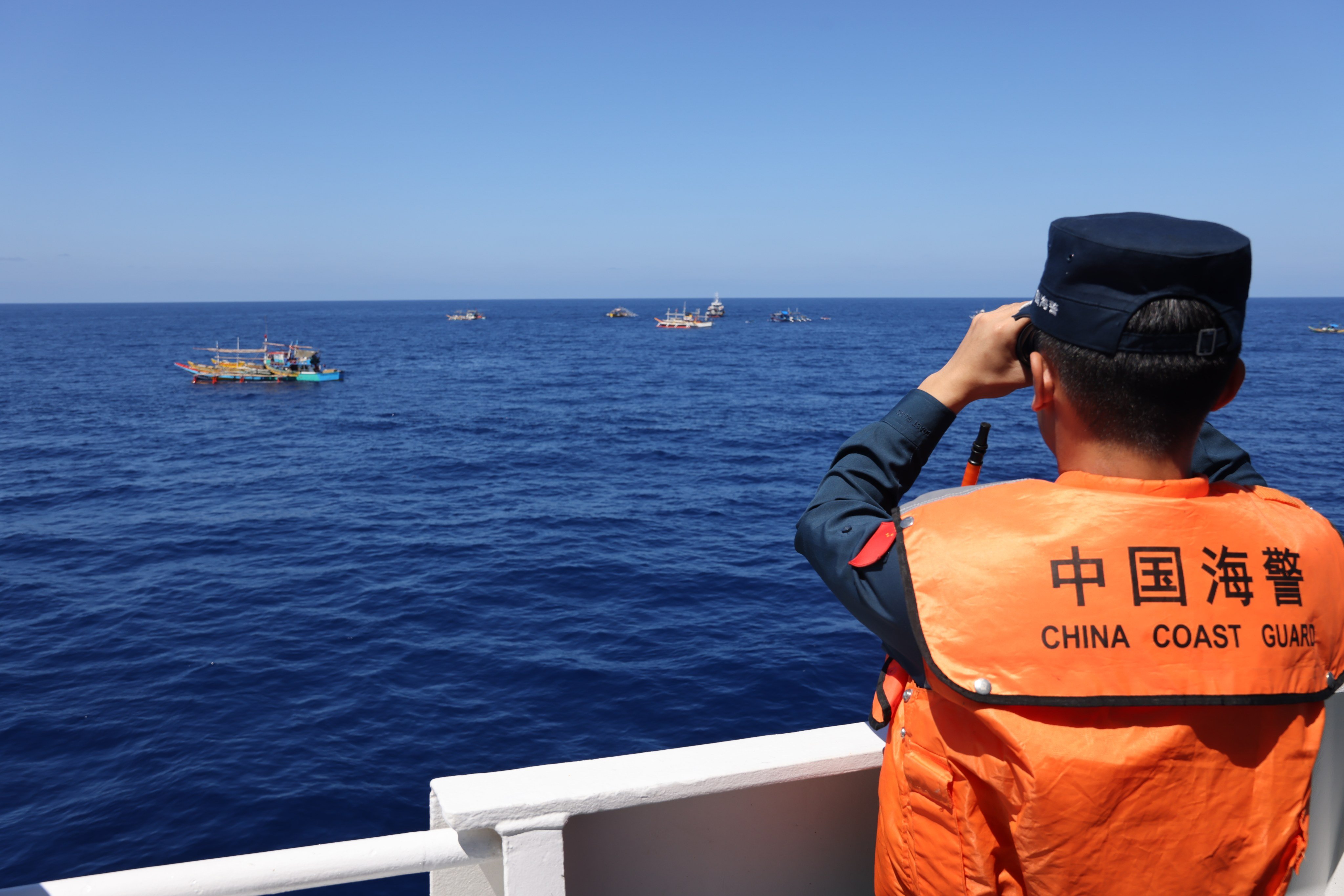 A law enforcer on a China Coast Guard vessel observes Philippine boats in a disputed area of the South China Sea in February. Photo: Handout via Xinhua
