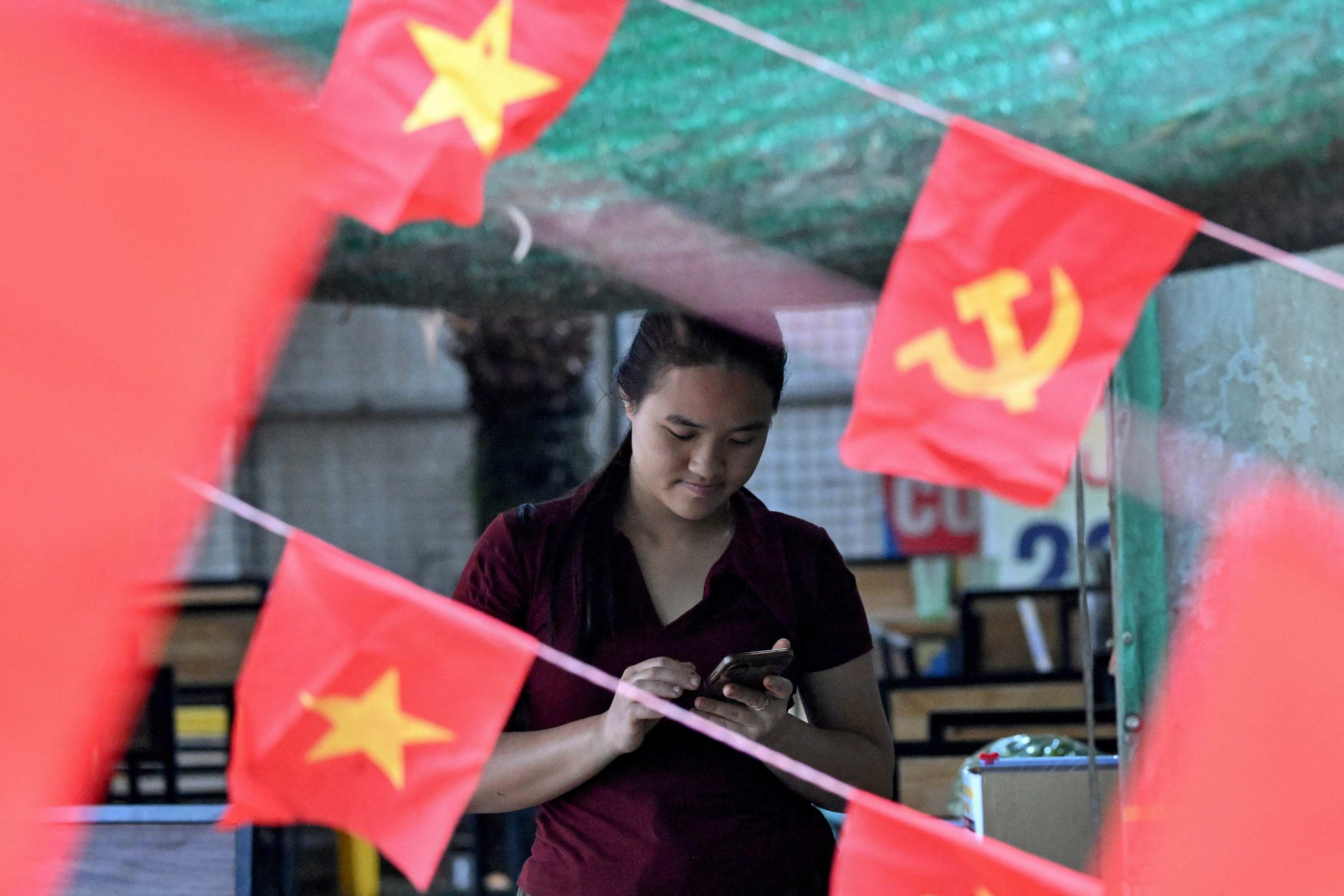 A girl checks her phone next to Communist Party and Vietnamese flags in Hanoi on February 27. Vietnam’s new artificial intelligence law went into effect on March 1. Photo: AFP