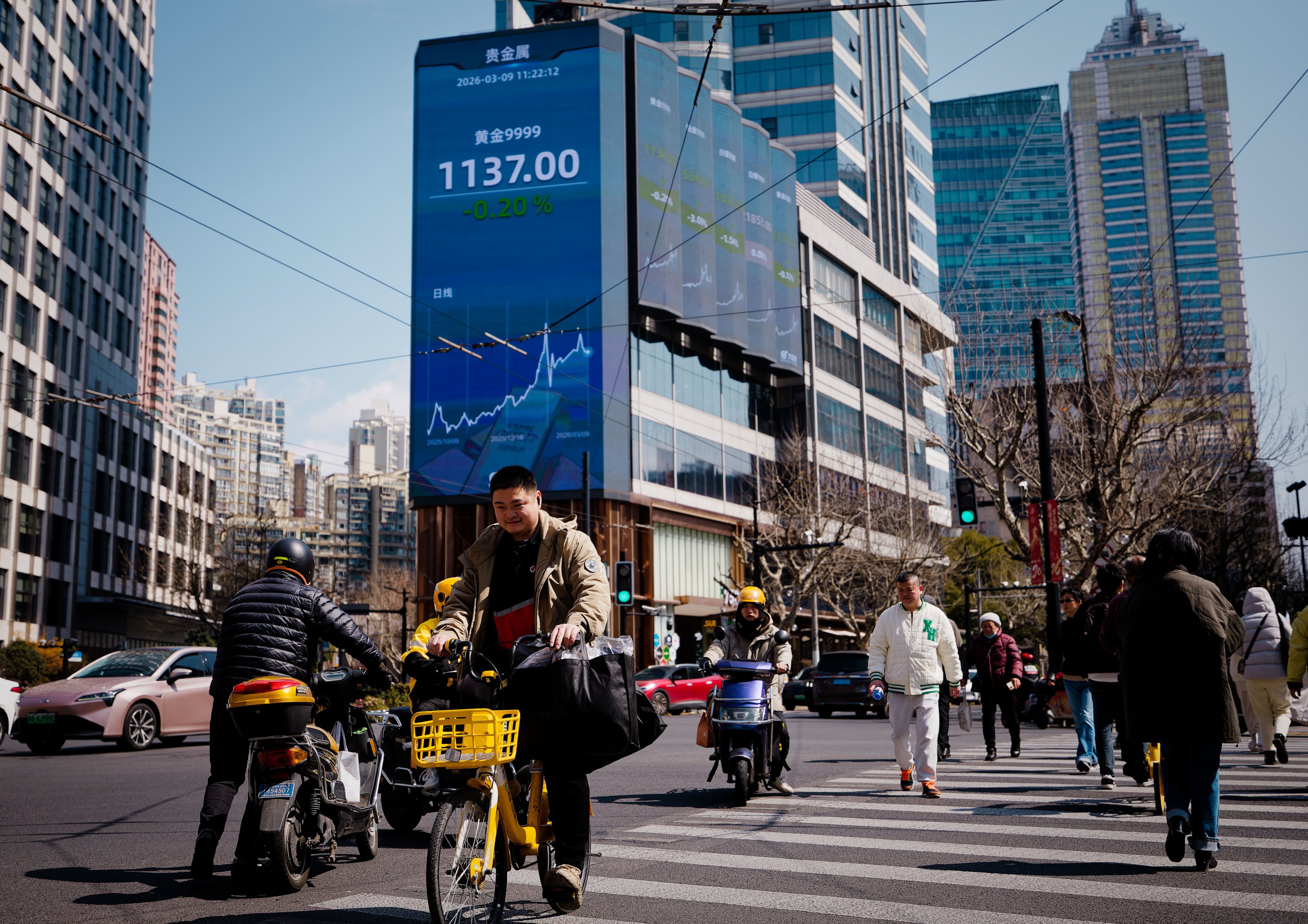 People cross the street beneath a screen showing stock exchange data in Shanghai on March 9, 2026. Photo: EPA