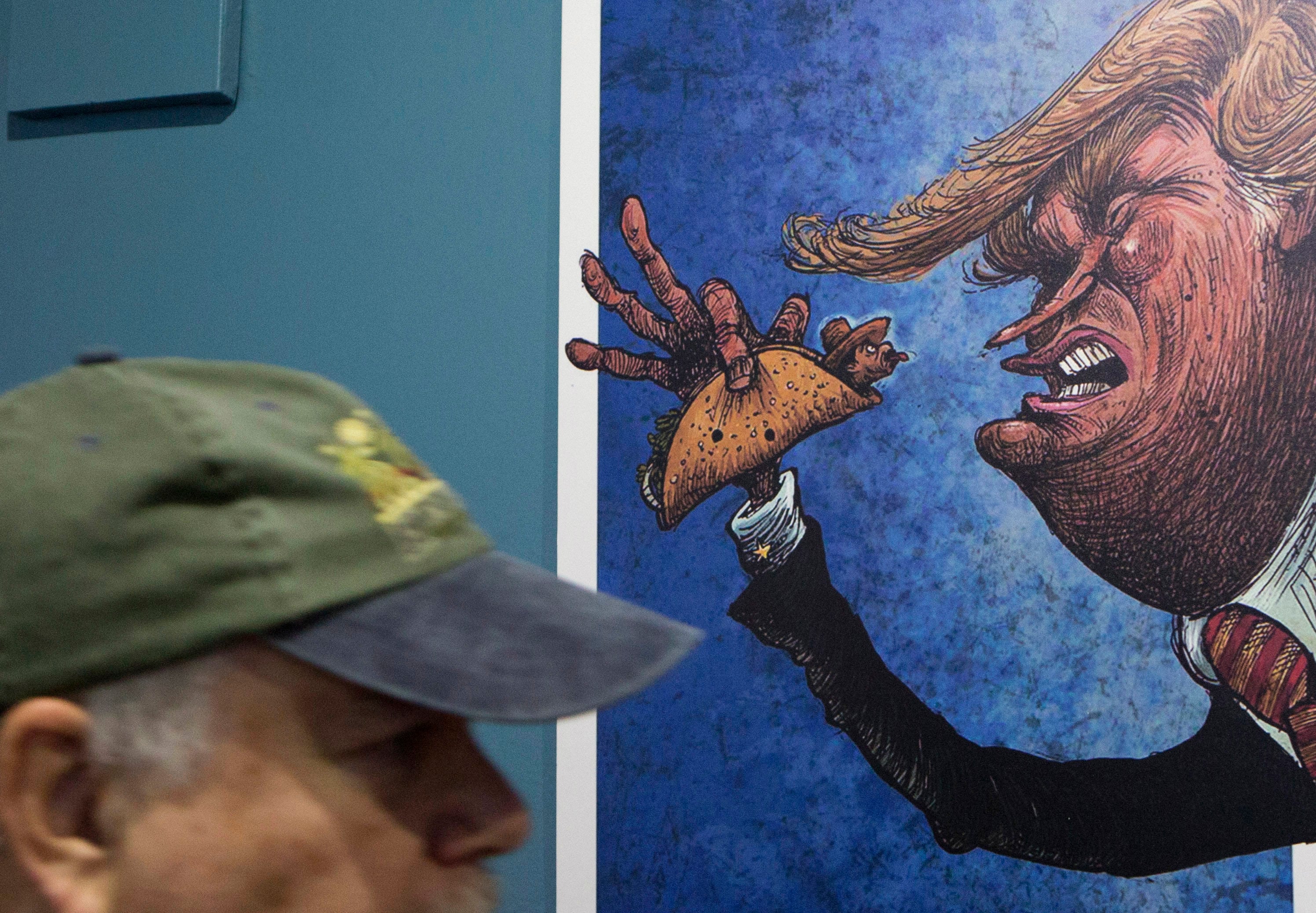 A visitor walks past a cartoon of Donald Trump holding a man wrapped in a taco at an exhibition at the Caricature Museum in Mexico City in November 2016. Photo: AP