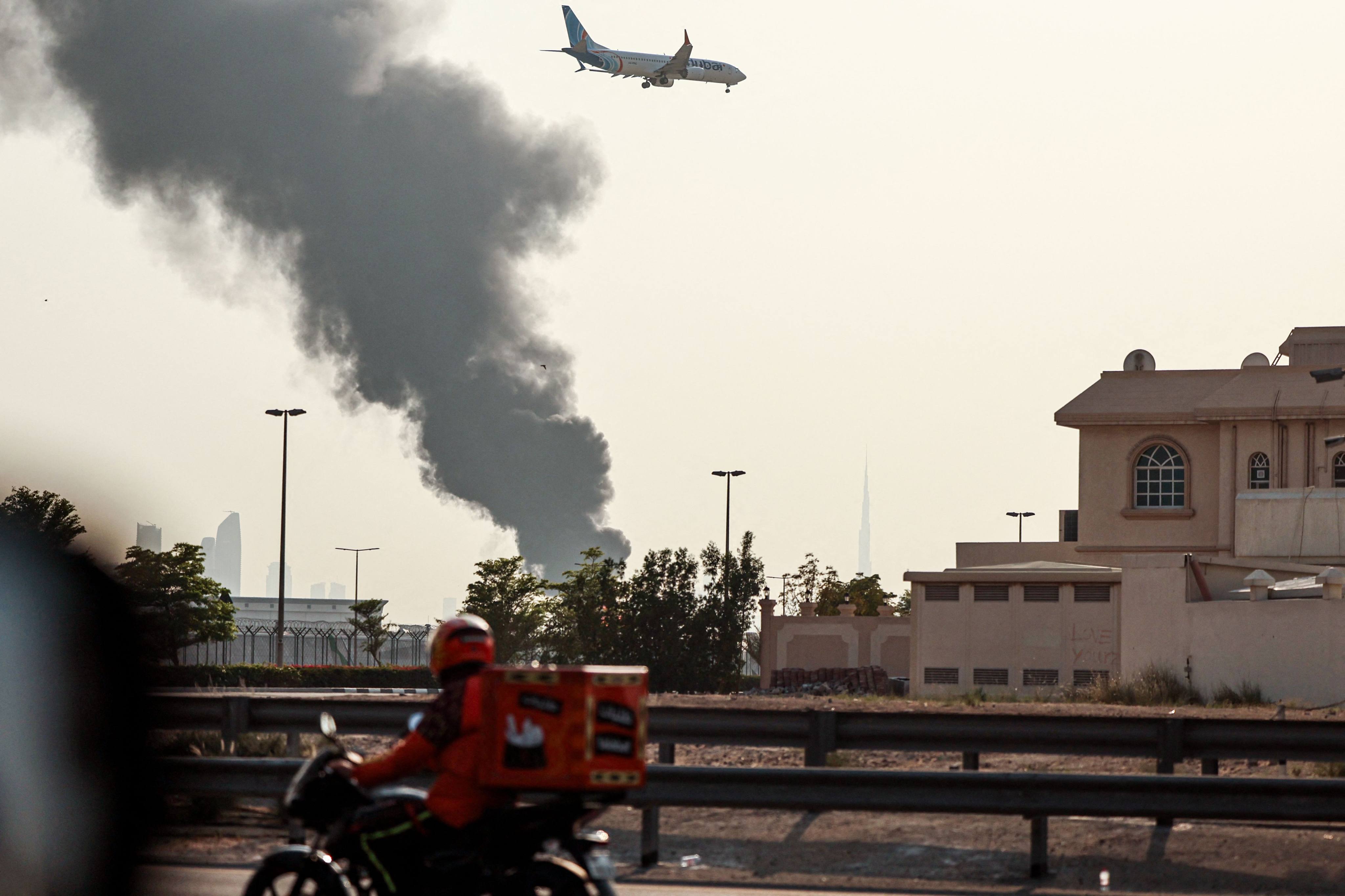 A delivery bike motors along a highway as a FlyDubai aircraft prepares to land while smoke rises from a fire near Dubai International Airport on March 16. Photo: AFP
