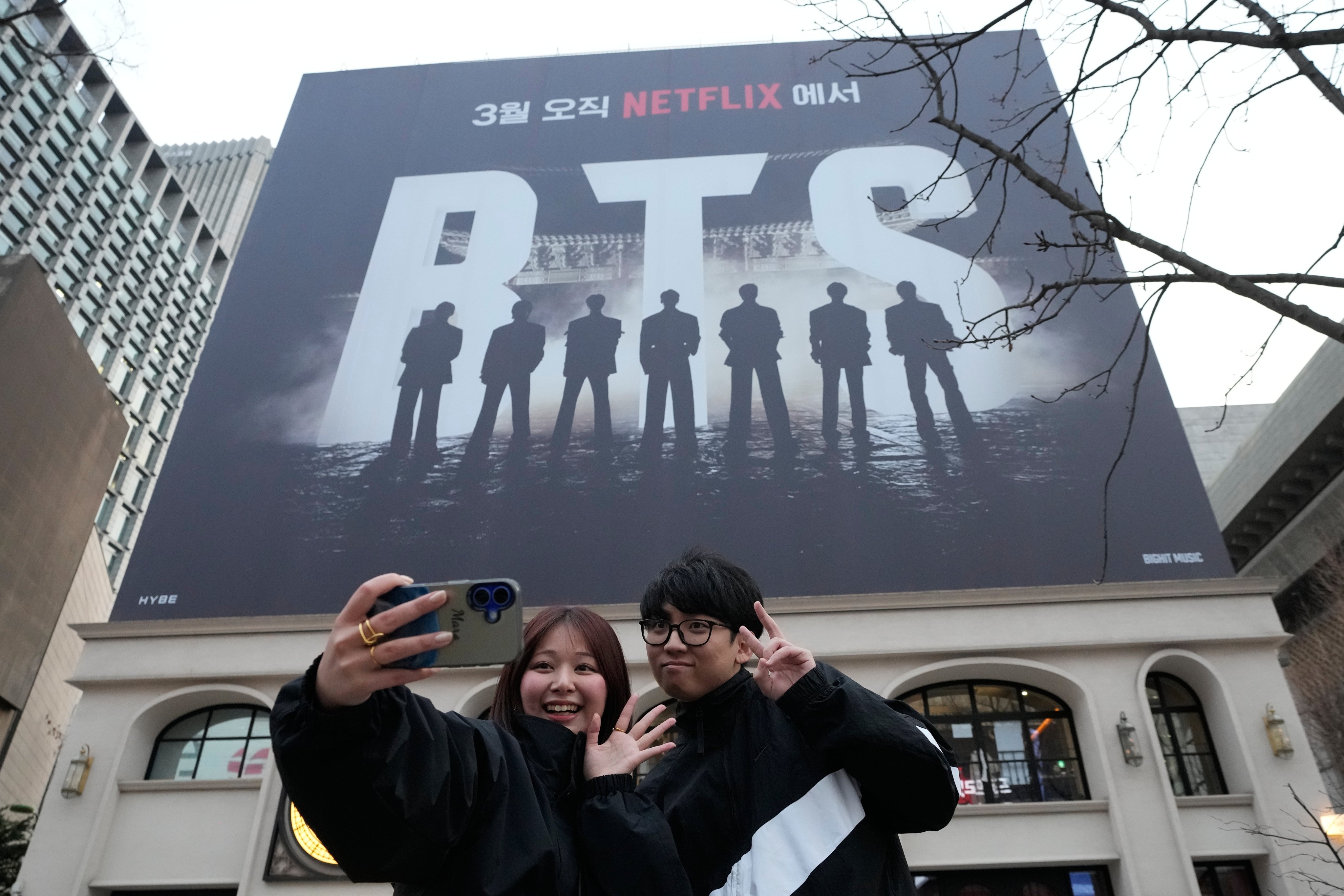 A couple takes a selfie photo near a banner promoting a comeback concert of K-pop group BTS at Gwanghwamun Square in Seoul, Wednesday, March 18, 2026. (AP Photo/Ahn Young-joon)