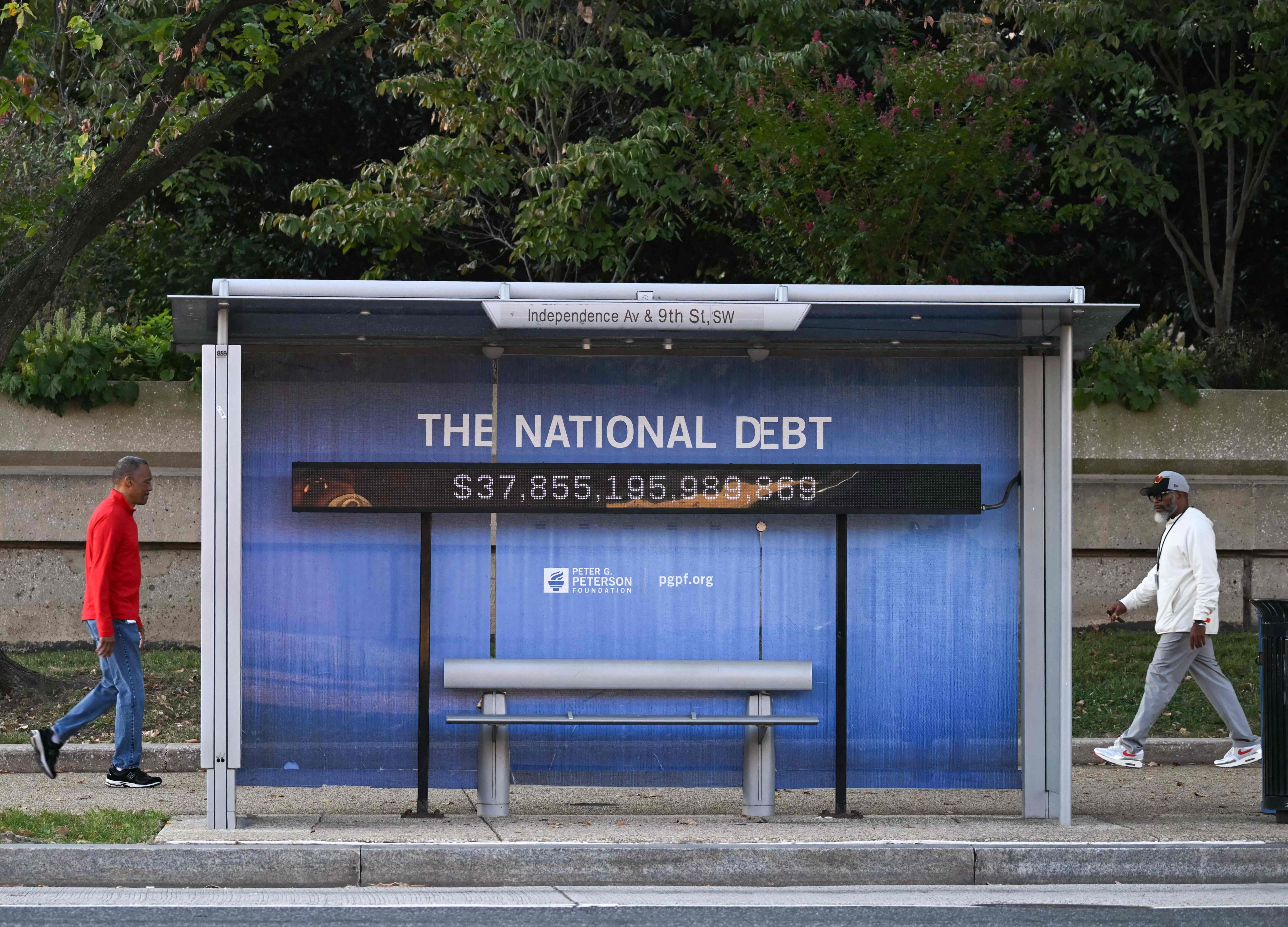 People walk past a bus stand displaying the US national debt  in Washington, DC on October 7, 2025. Photo: AFP