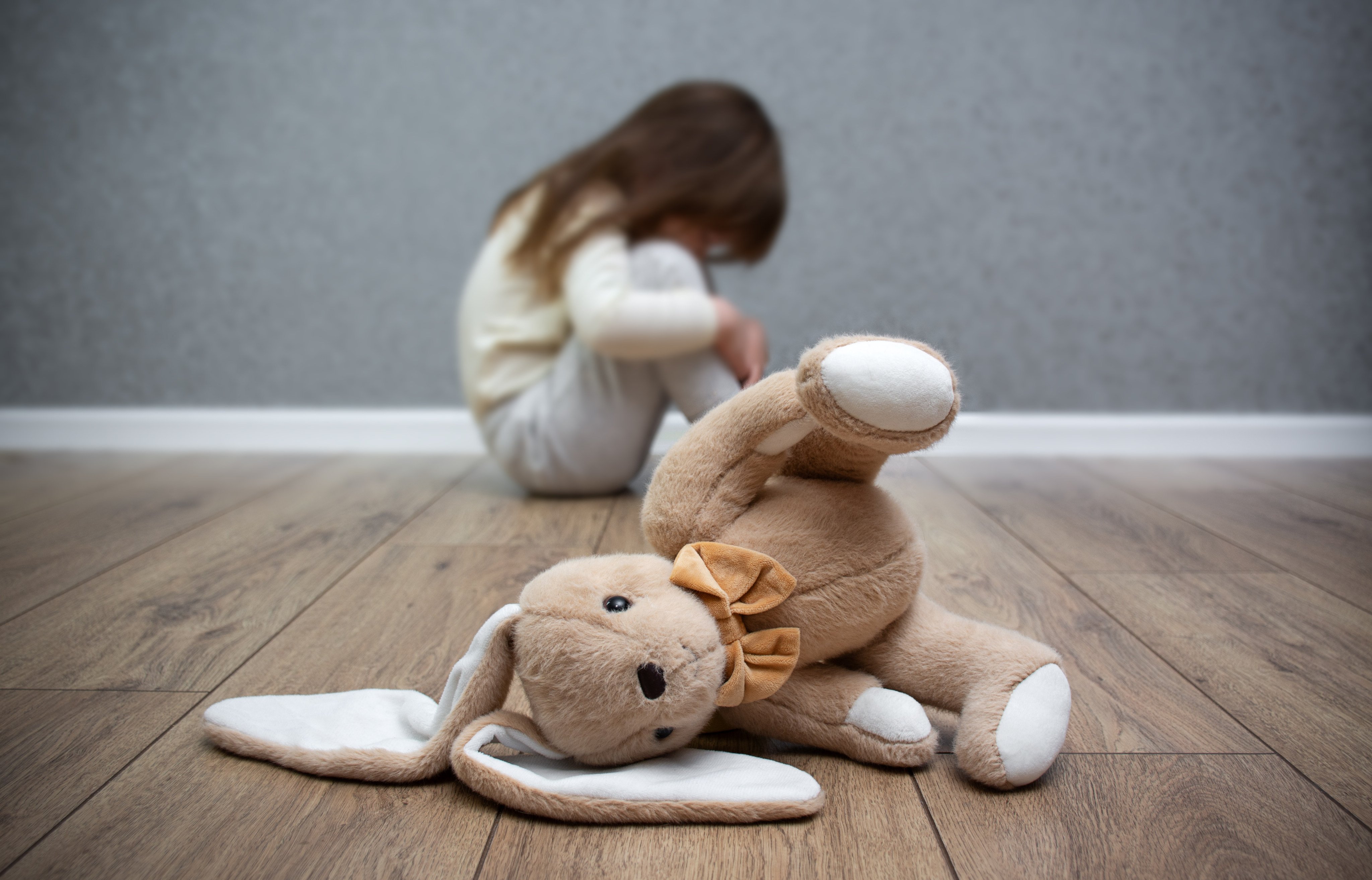 A stuffed bunny on the floor, a scared child sitting behind it. Child abuse. Bullying in the family. Photo: Getty Images