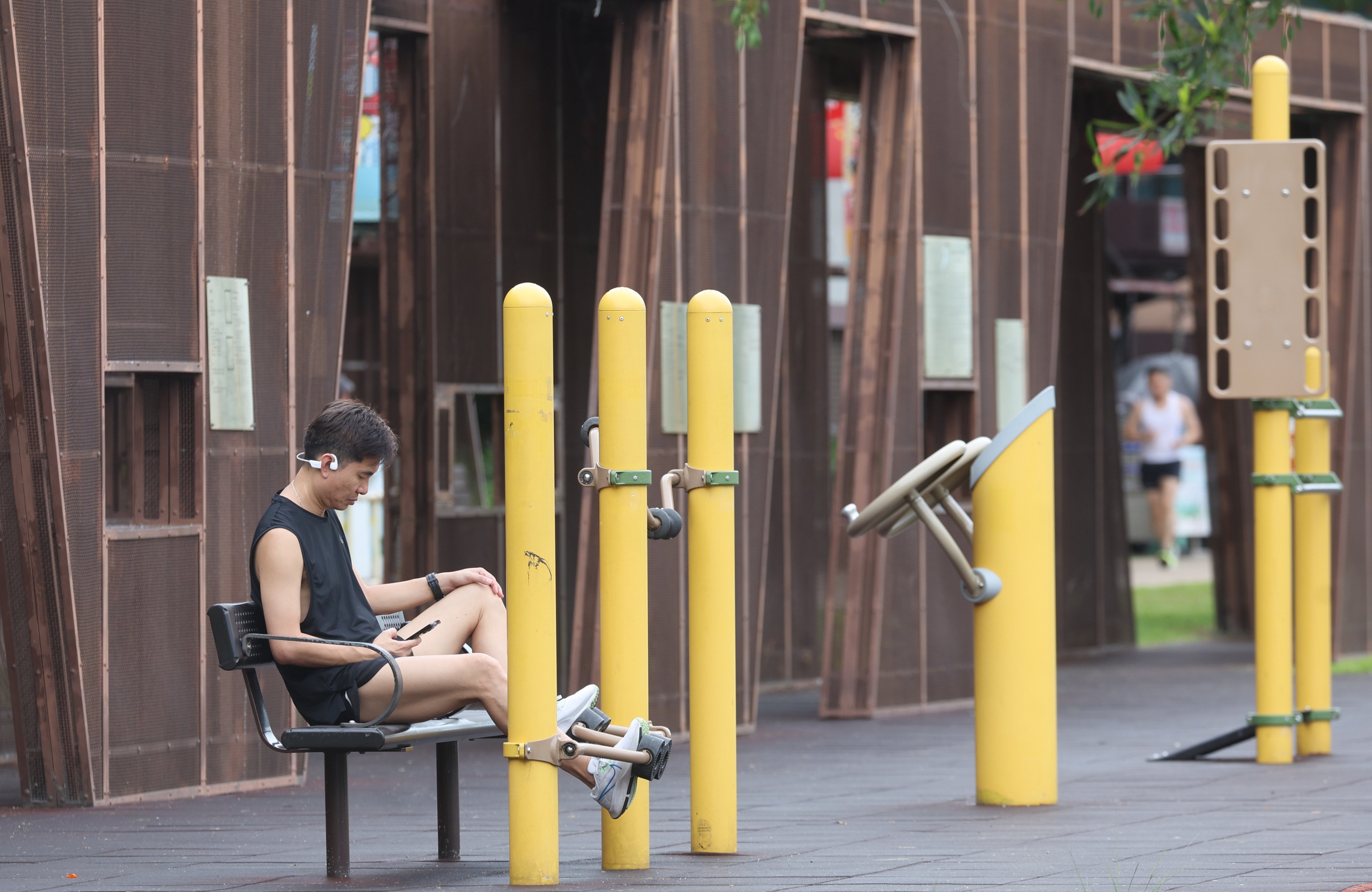 A man checks his phone while using exercise equipment at the Kwun Tong promenade in July 2024. Photo: Edmond So