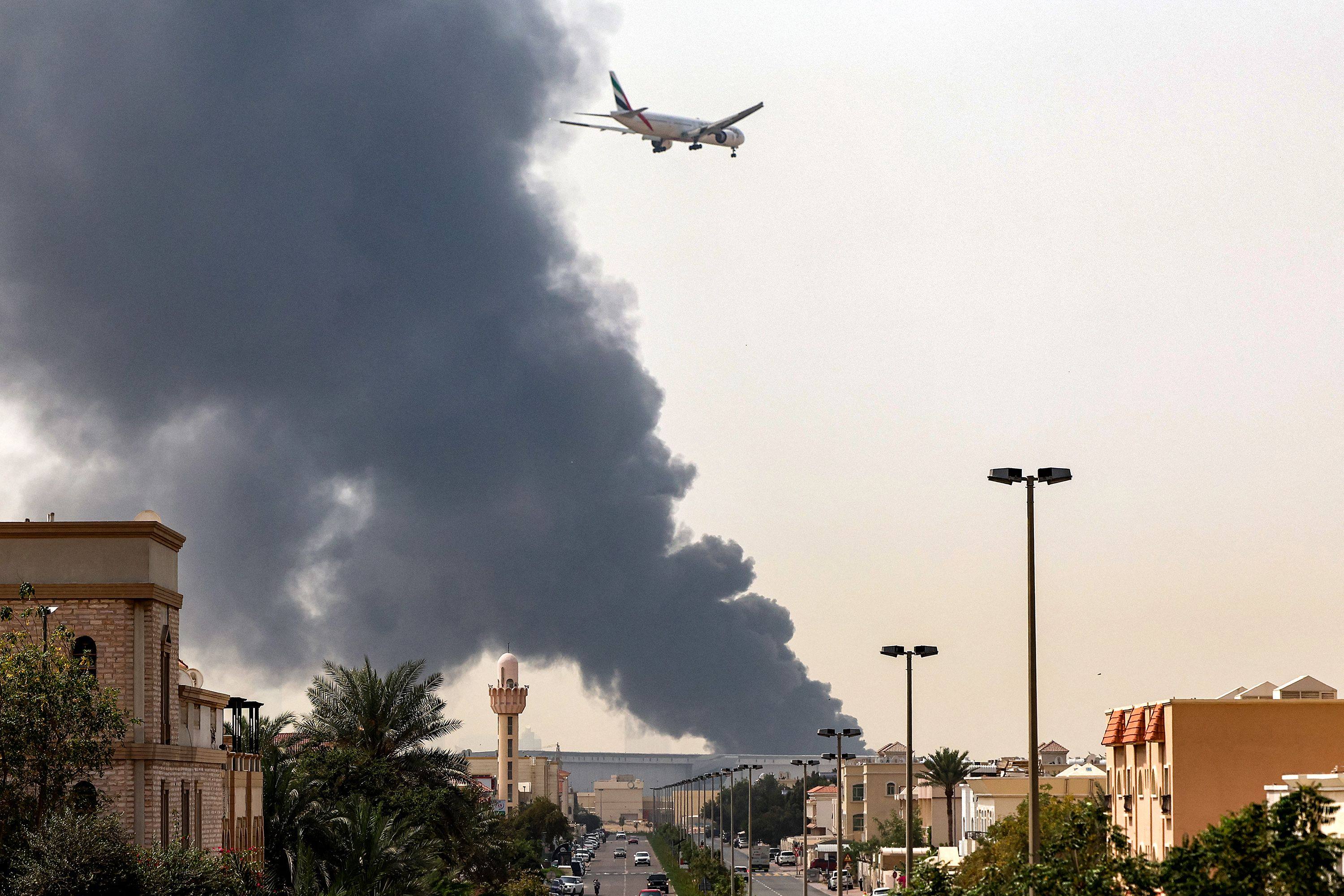 An aircraft prepares for landing as a smoke plume rises from a fire near Dubai International Airport on March 16. Photo: AFP