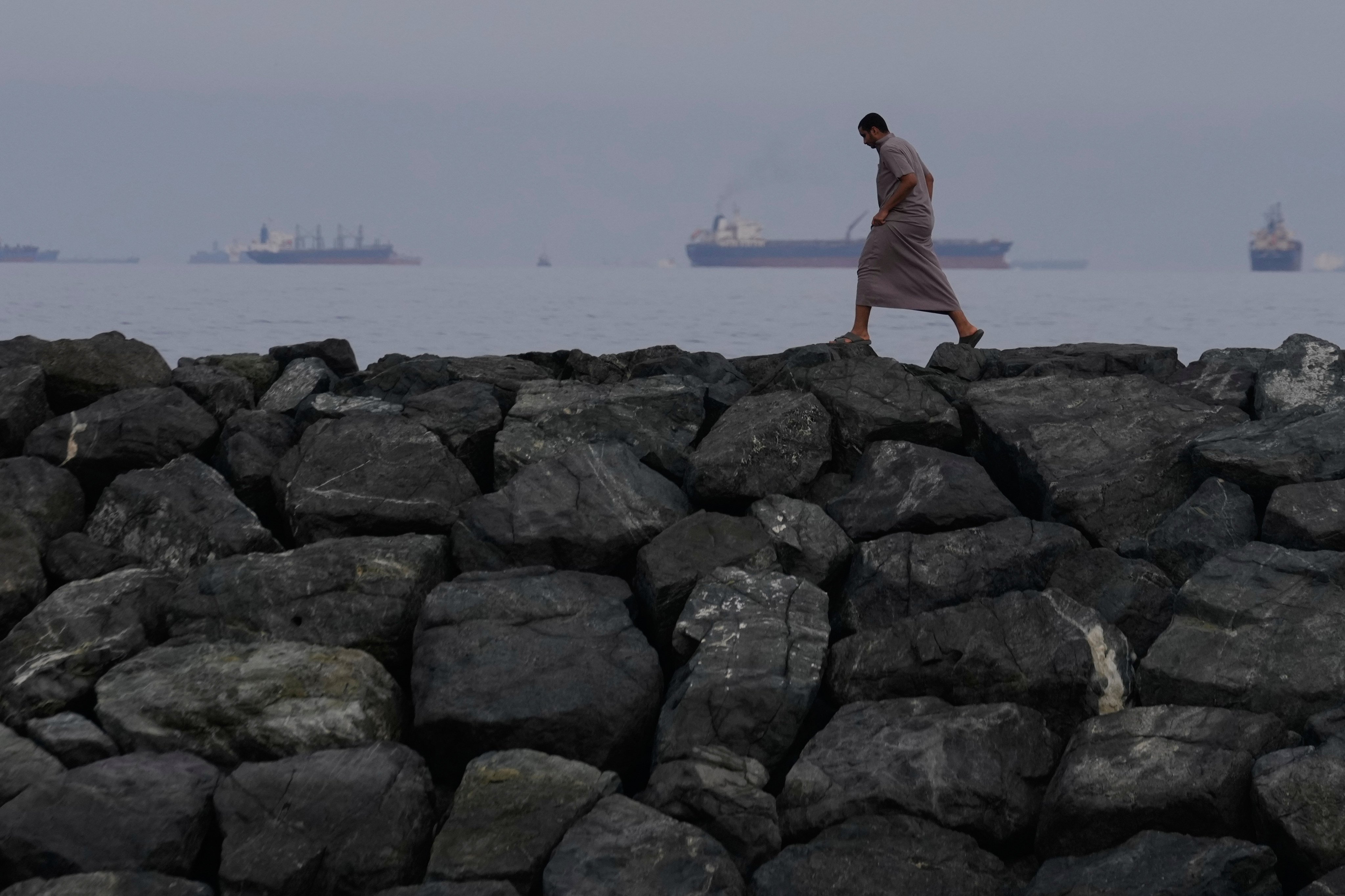 A man walks along rocks as oil tankers and cargo ships line up in the Strait of Hormuz, seen from Khor Fakkan in the United Arab Emirates on March 11. Photo: AP