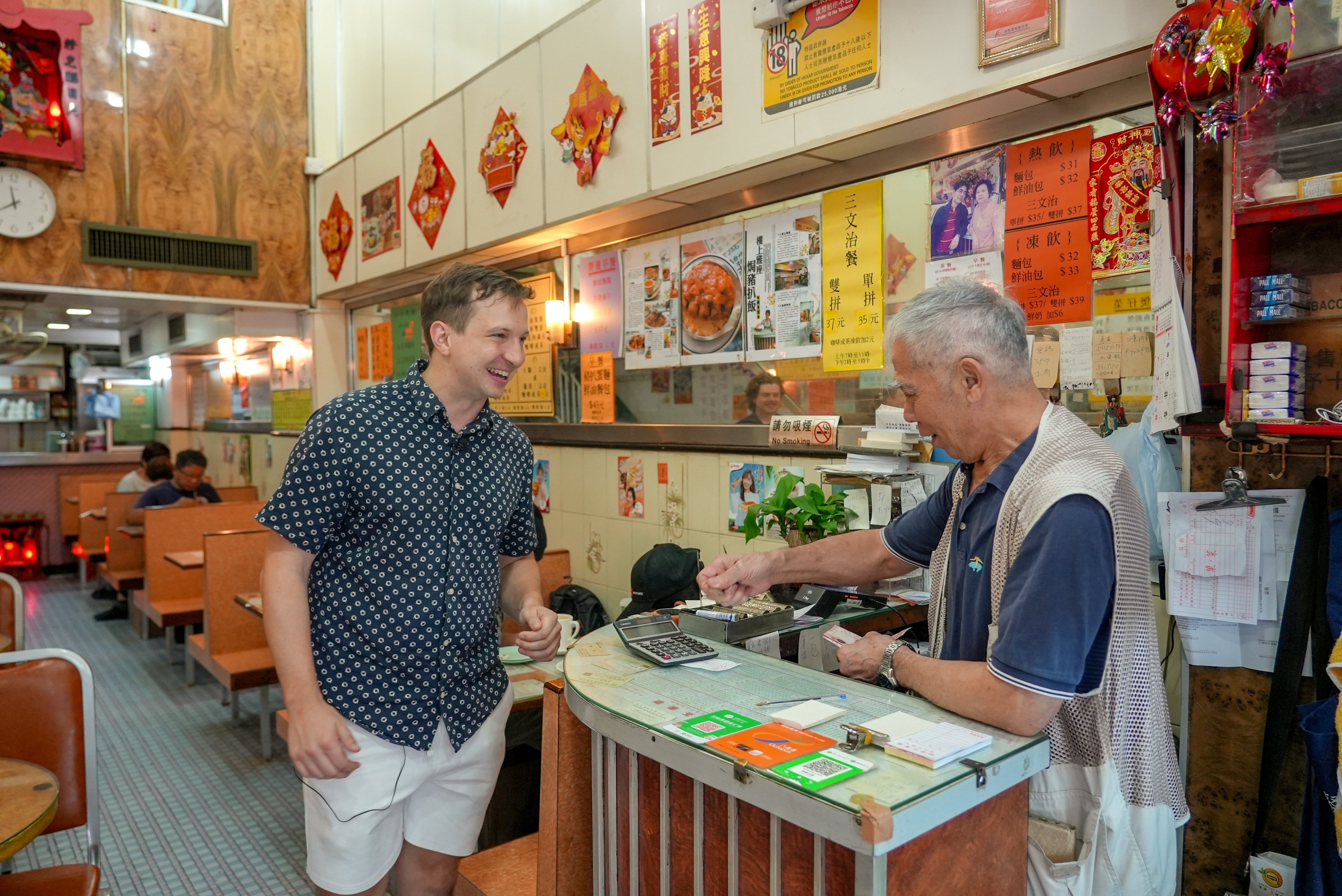 Jonas Groom laughs with the owner of a cha chaan teng in Sai Ying Pun as he pays for his meal on September 22, 2025. Photo: Sophie Li
