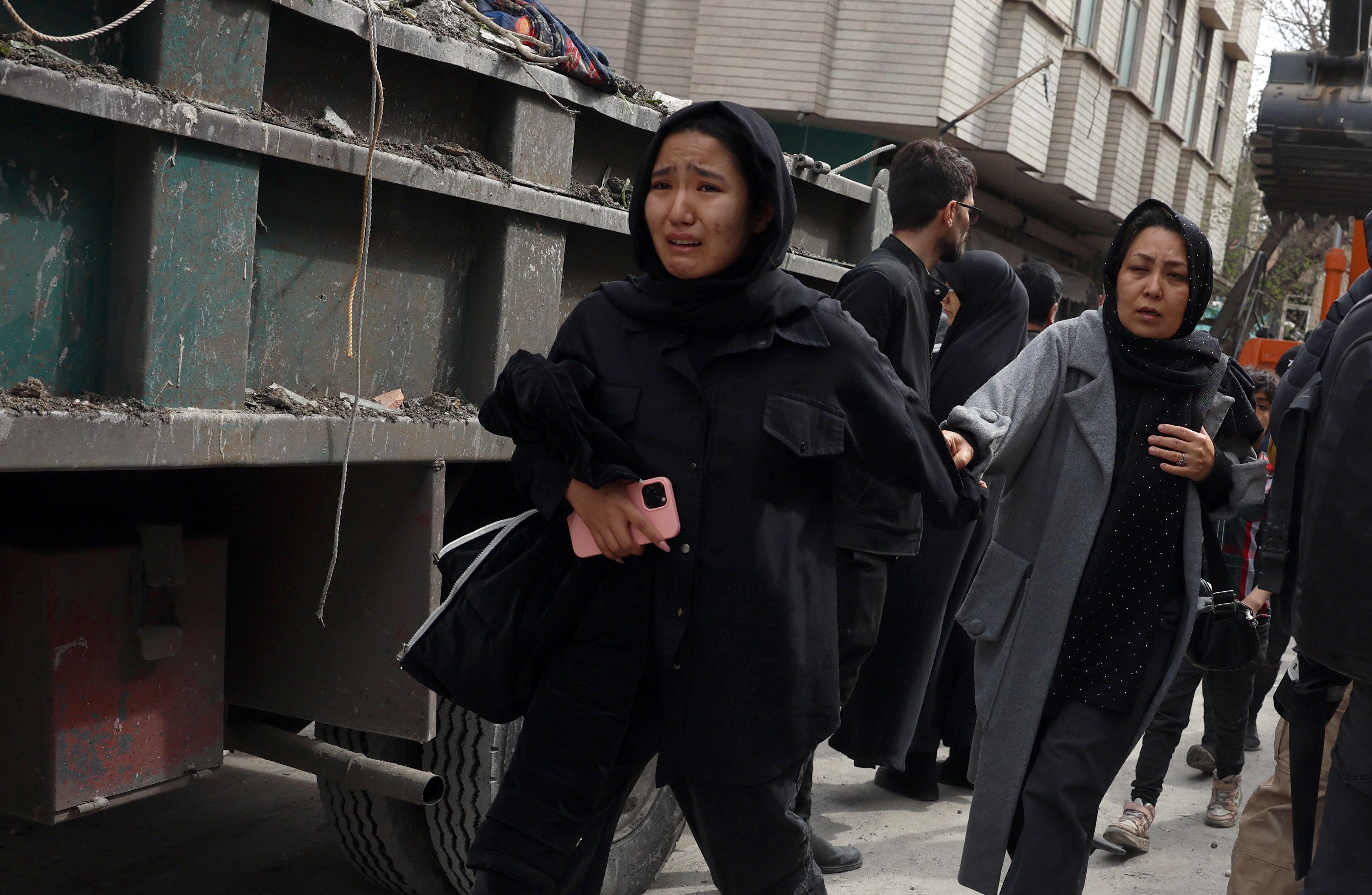 People hurry past damaged residential buildings in southern Tehran, on March 27. Photo: EPA