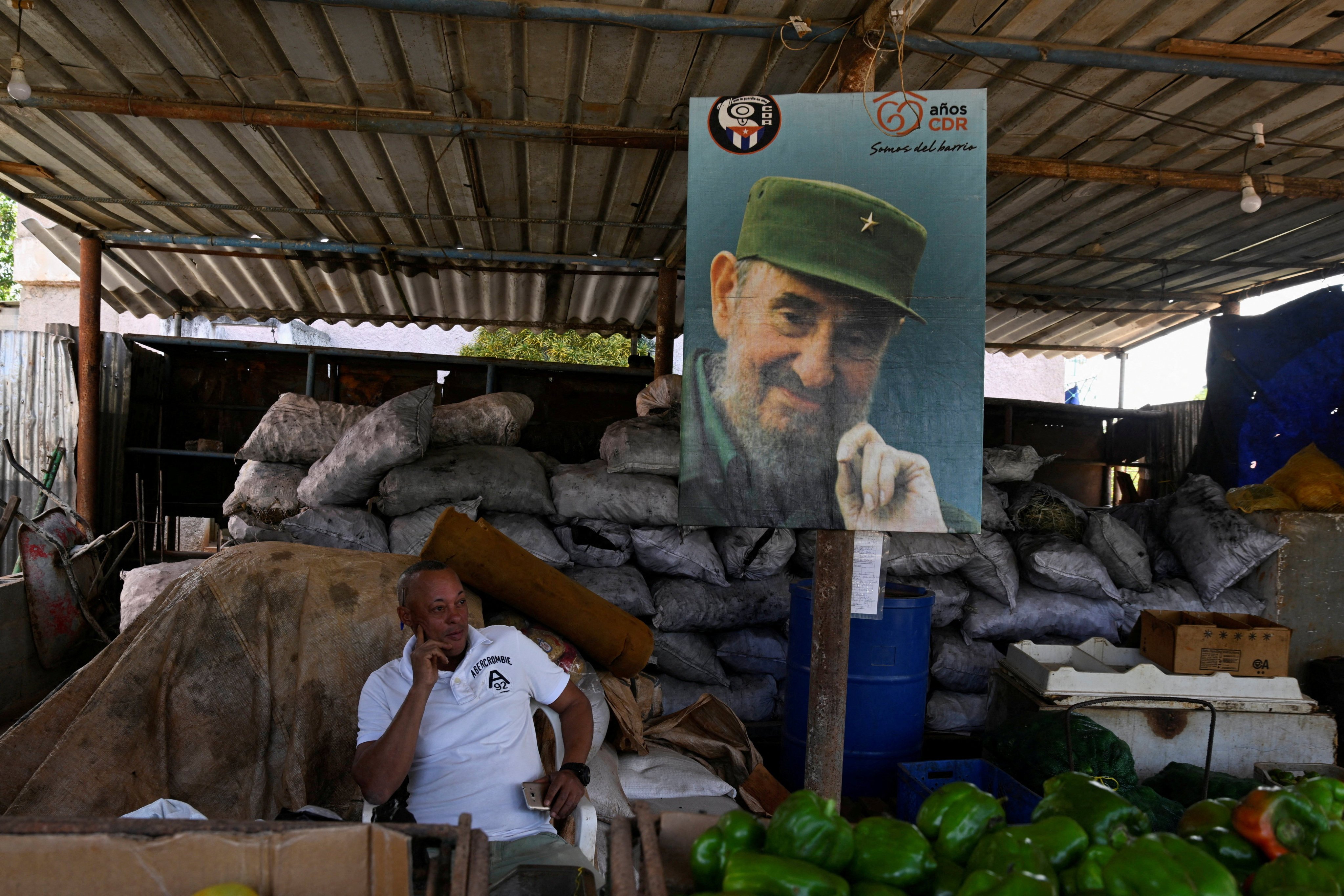 A charcoal seller in Havana waits for customers while sitting next to a poster of the late Cuban revolution leader Fidel Castro. Photo: Reuters