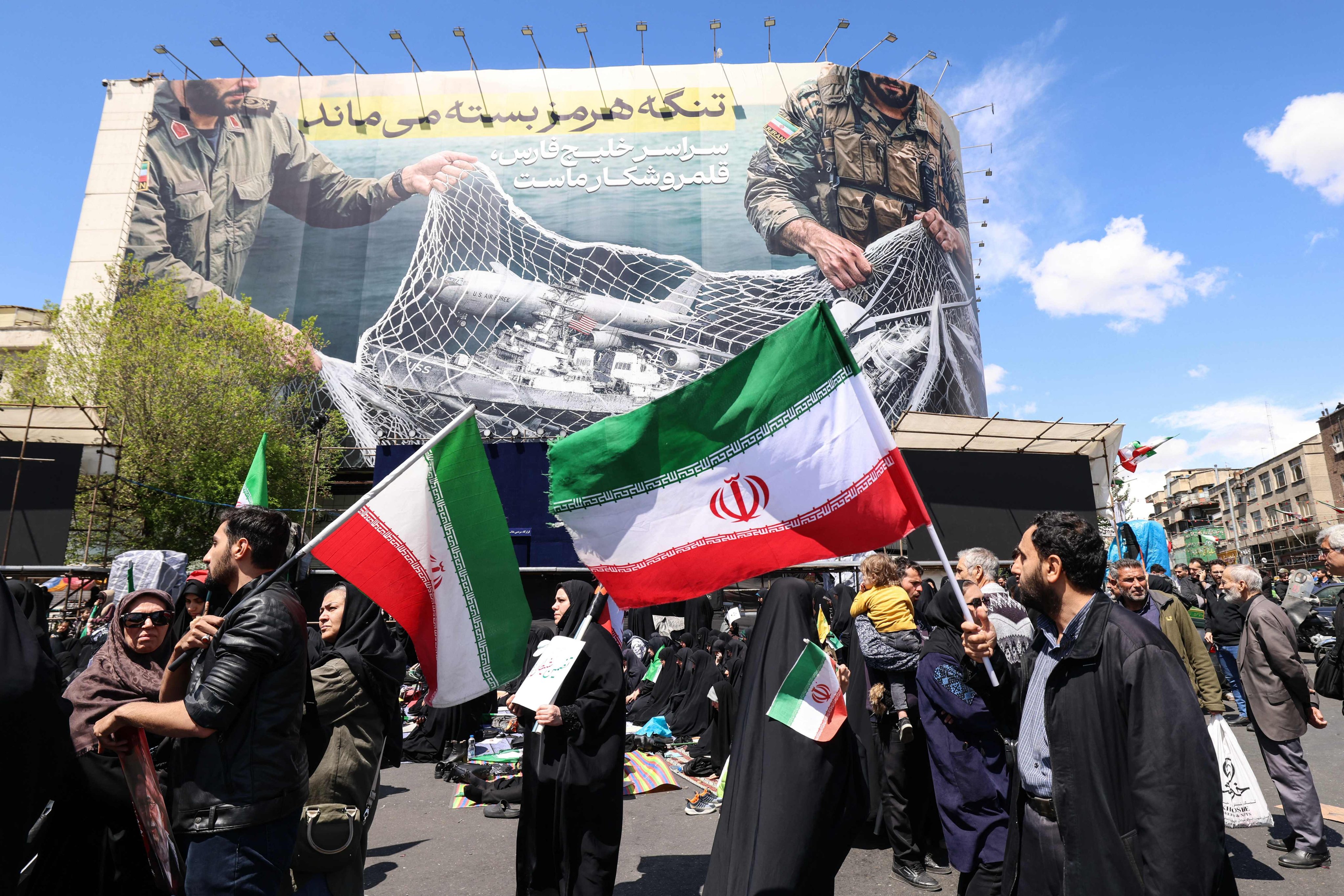 Iranians wave national flags beneath a large billboard in Tehran’s Revolution Square on Wednesday, following the announcement that the United States and Iran have agreed to a two-week ceasefire. Photo: AFP