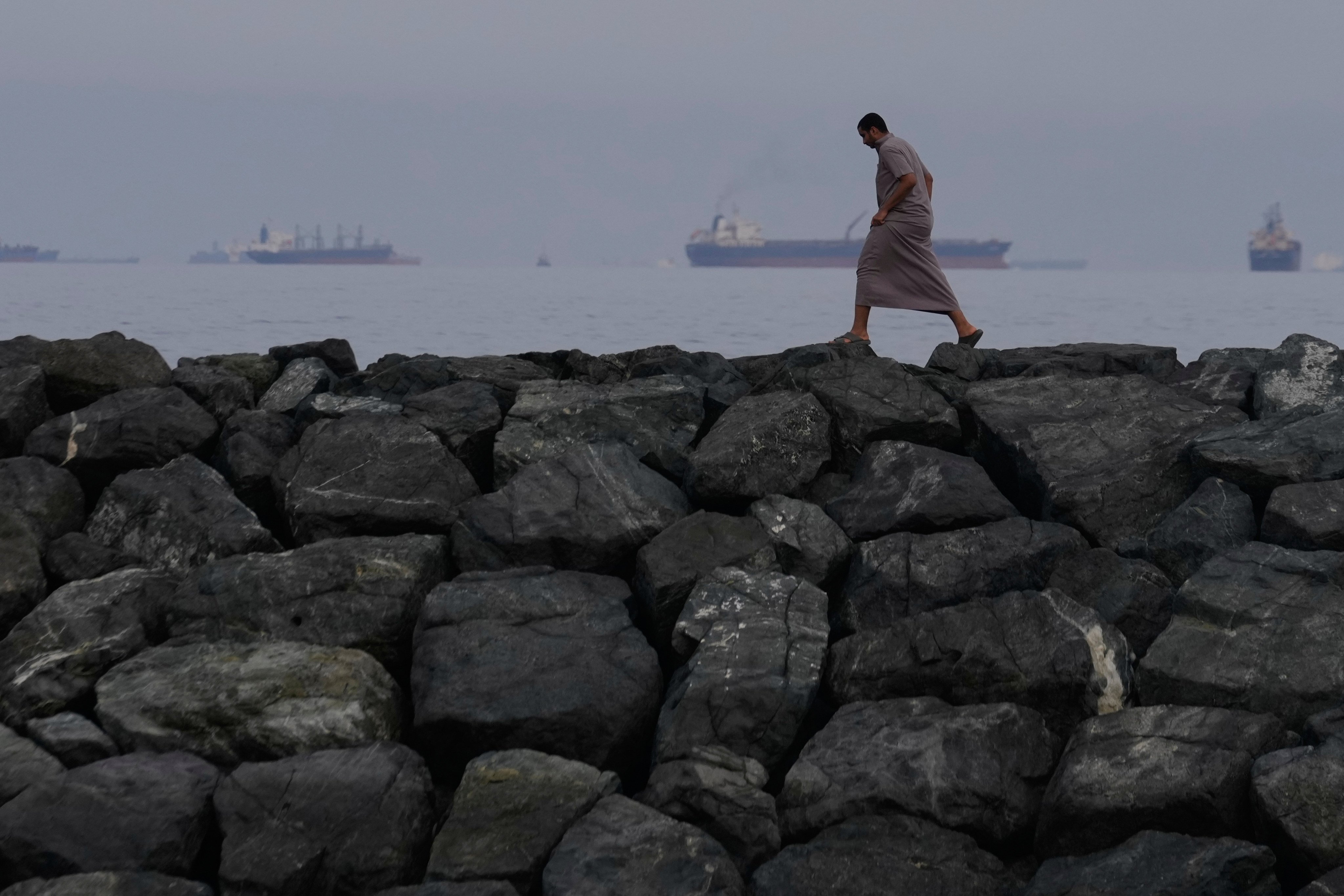 A man walks along the shore as oil tankers and cargo ships line up in the Strait of Hormuz, as seen from Khor Fakkan, United Arab Emirates. Photo: AP