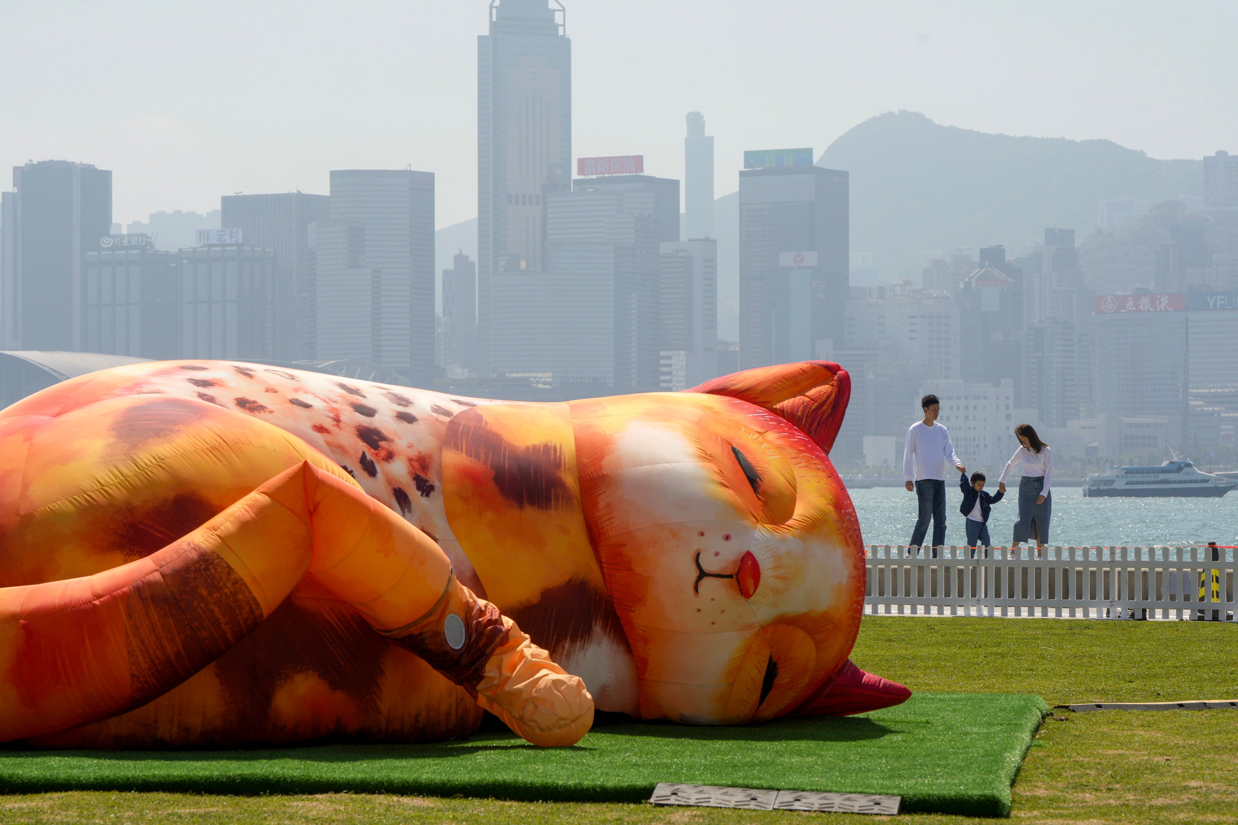 A family walks along the harbour on March 15, past a giant inflatable sleeping cat in the Art Park in the West Kowloon Cultural District. Photo: Sam Tsang