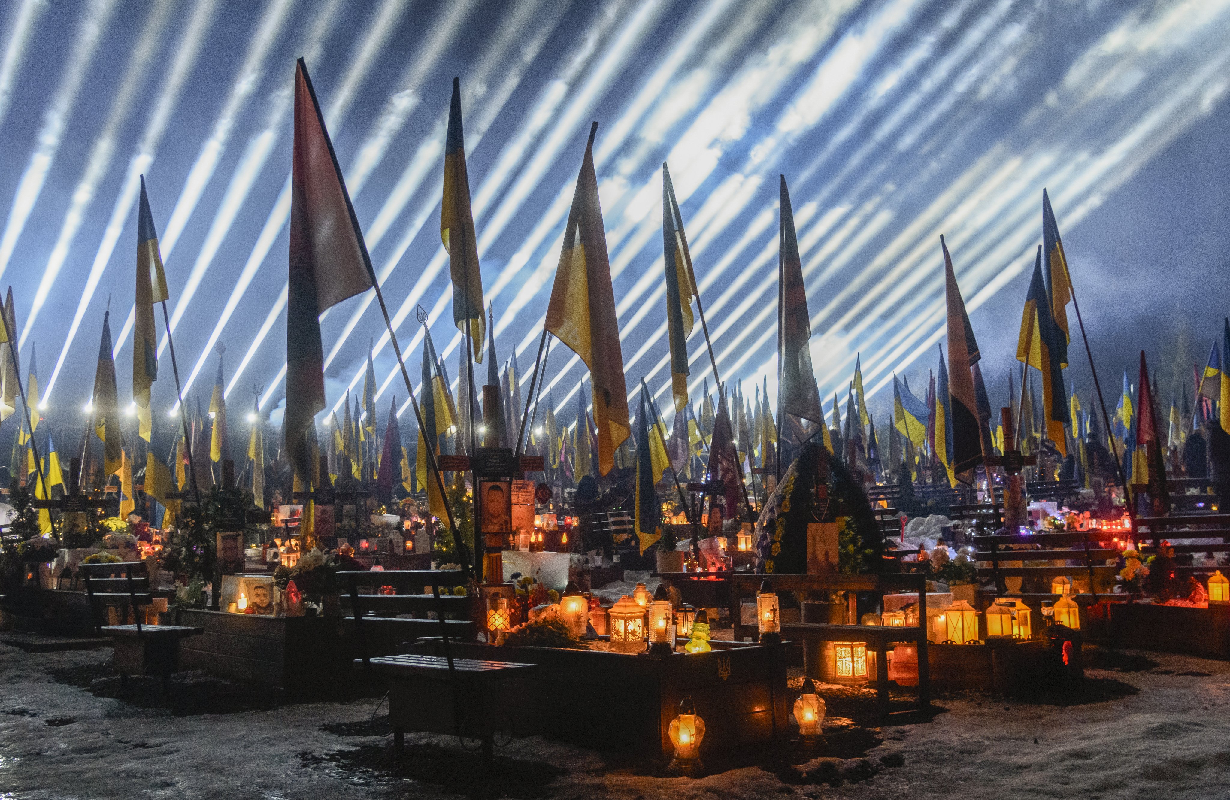 Beams of light illuminate the sky over the graves of fallen Ukrainian soldiers as friends and relatives take part in a joint prayer and candlelight vigil at Lychakiv Military Cemetery in Lviv, western Ukraine, on February 23. Photo: EPA