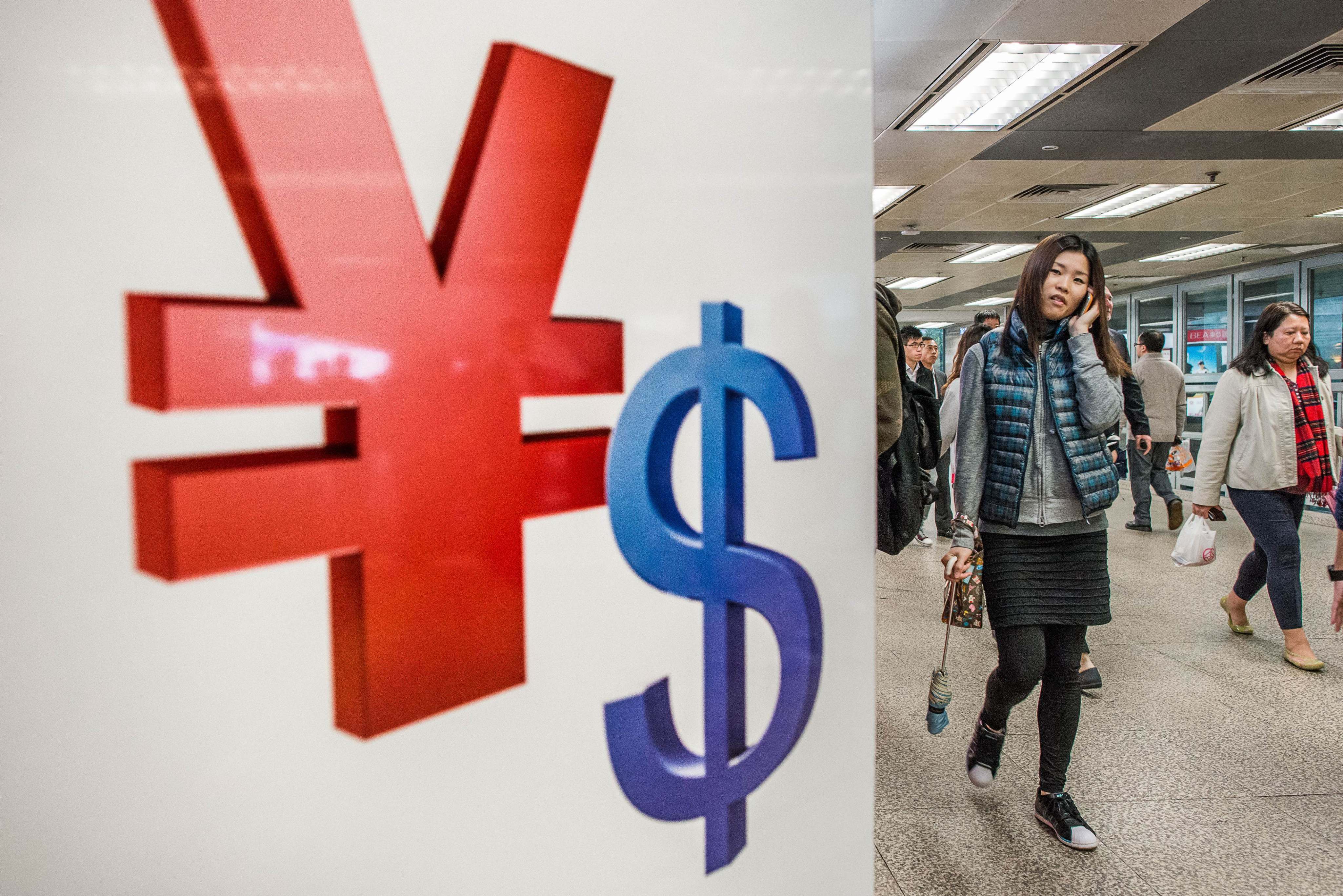 People walk past Chinese yuan and US dollar symbols in Hong Kong. Former PBOC governor Zhou Xiaochuan says China should seize fresh opportunities to promote the yuan as an international currency. Photo: AFP