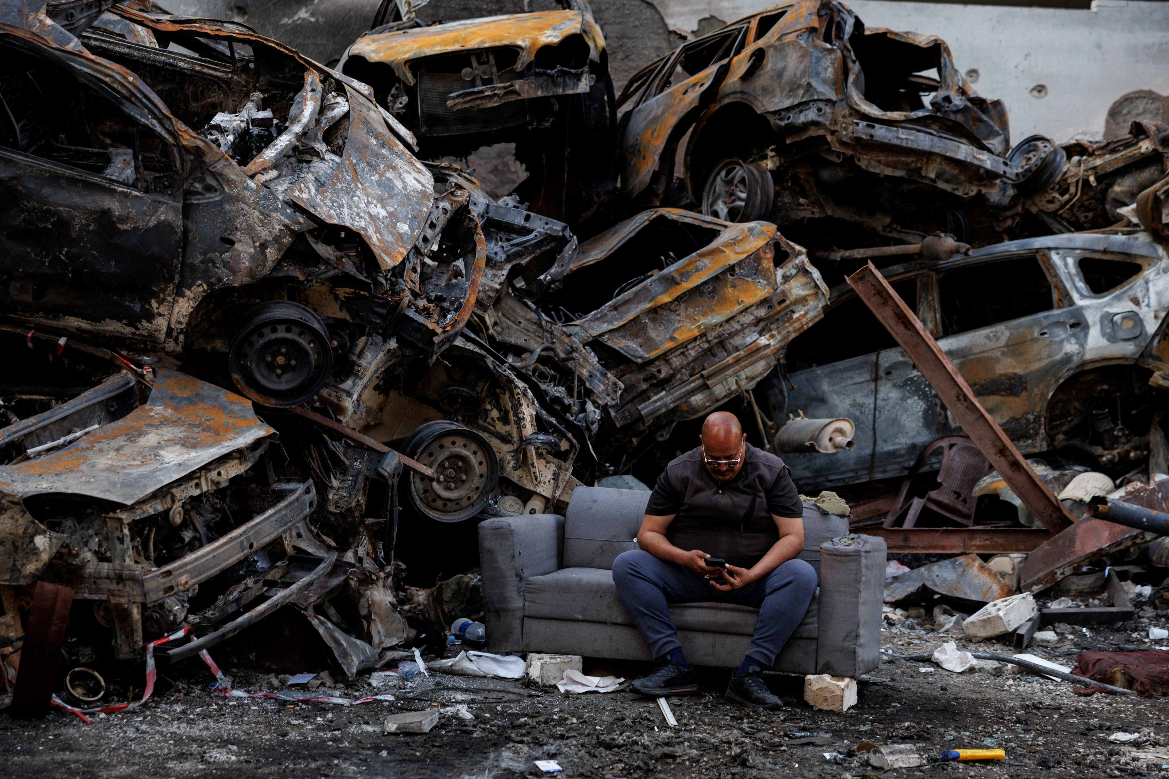 A man who said he survived an Israeli strike sits among piled damaged cars in Beirut. Photo: Reuter
