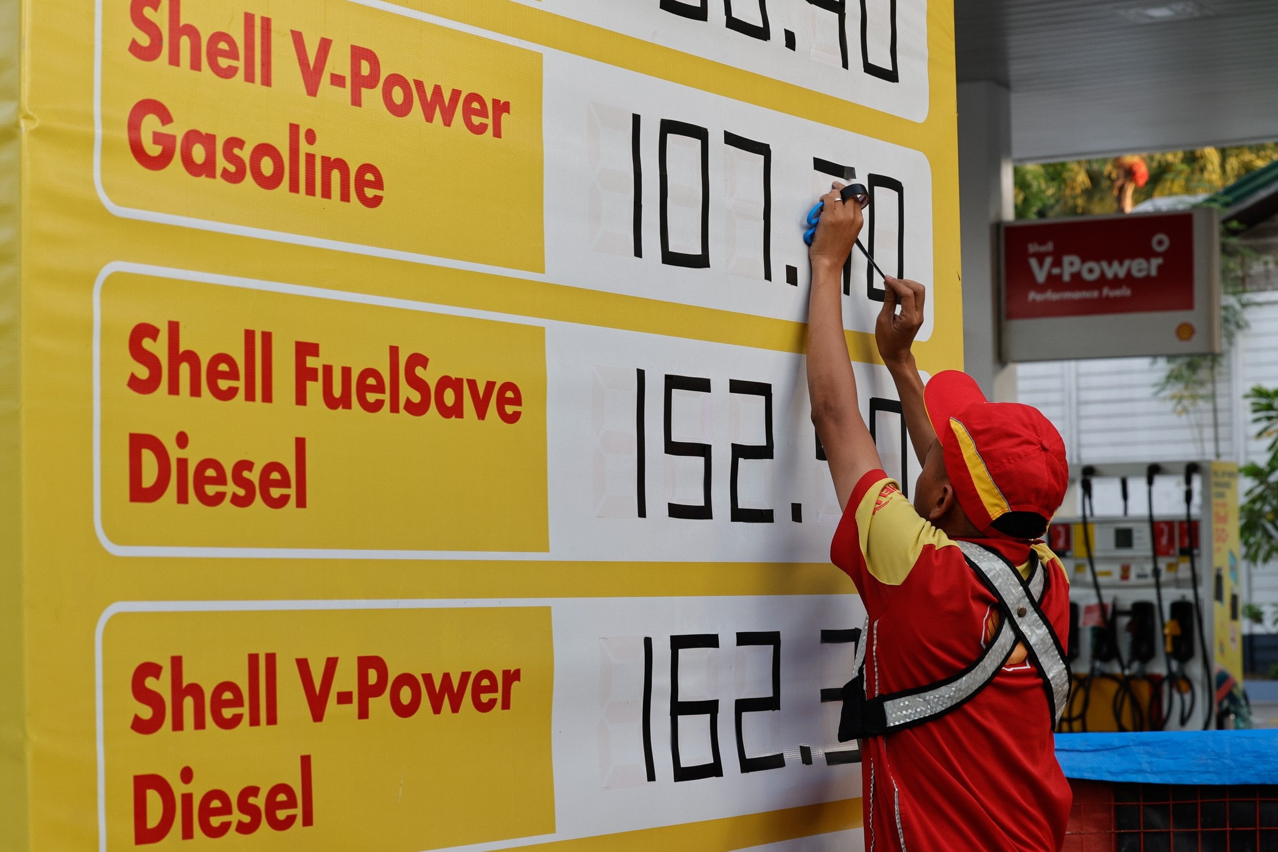 A pump attendant uses adhesive tape to change figures of fuel prices in Quezon City on April 7. Photo:    EPA