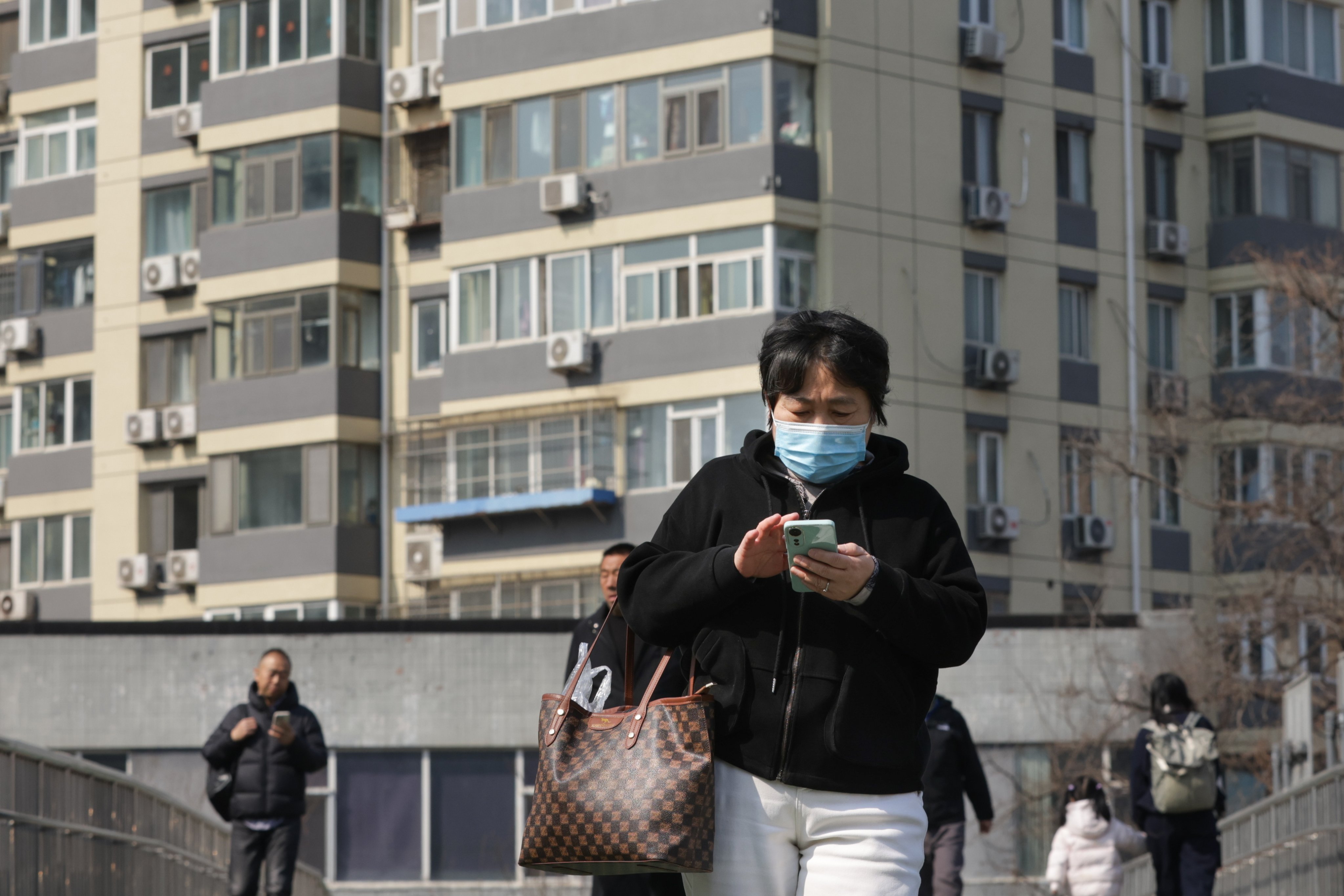 People walk past condominium buildings in Beijing on March 16, 2026. Photo: EPA