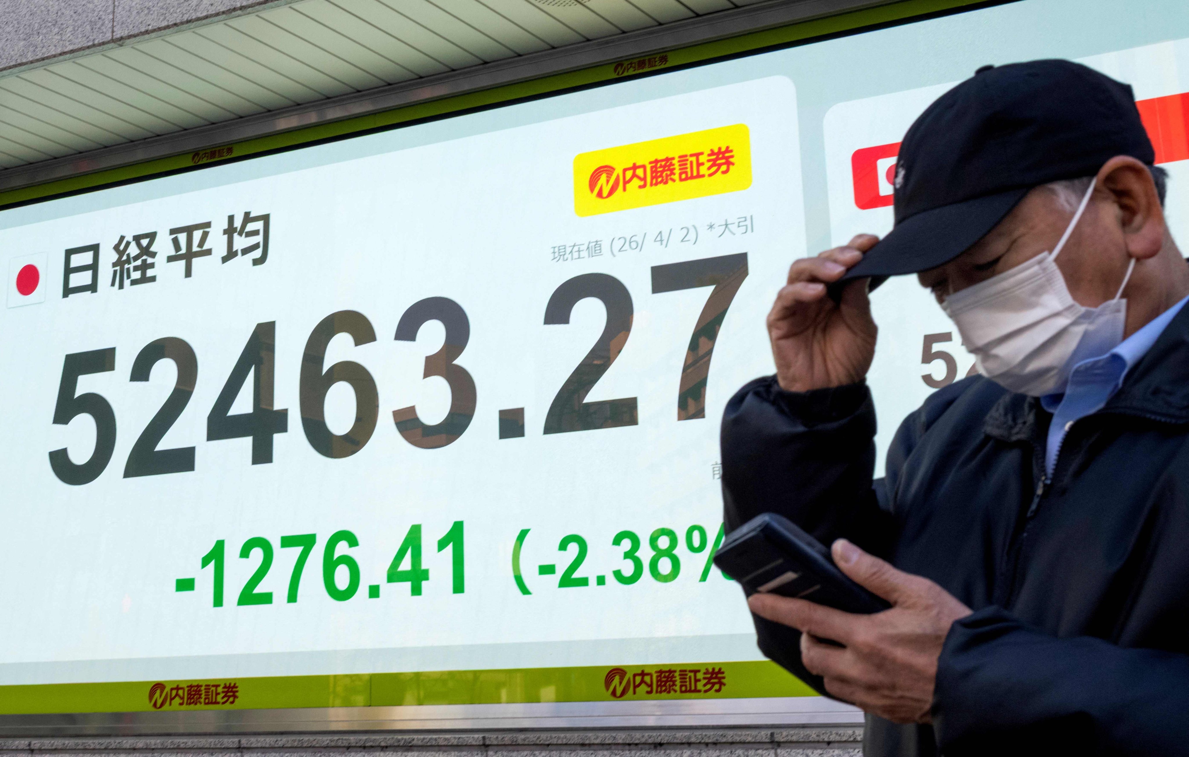 A man stands in front of an electronic board displaying the closing numbers of the Nikkei Stock Average on the Tokyo Stock Exchange, in Tokyo, on April 2. Photo: AFP