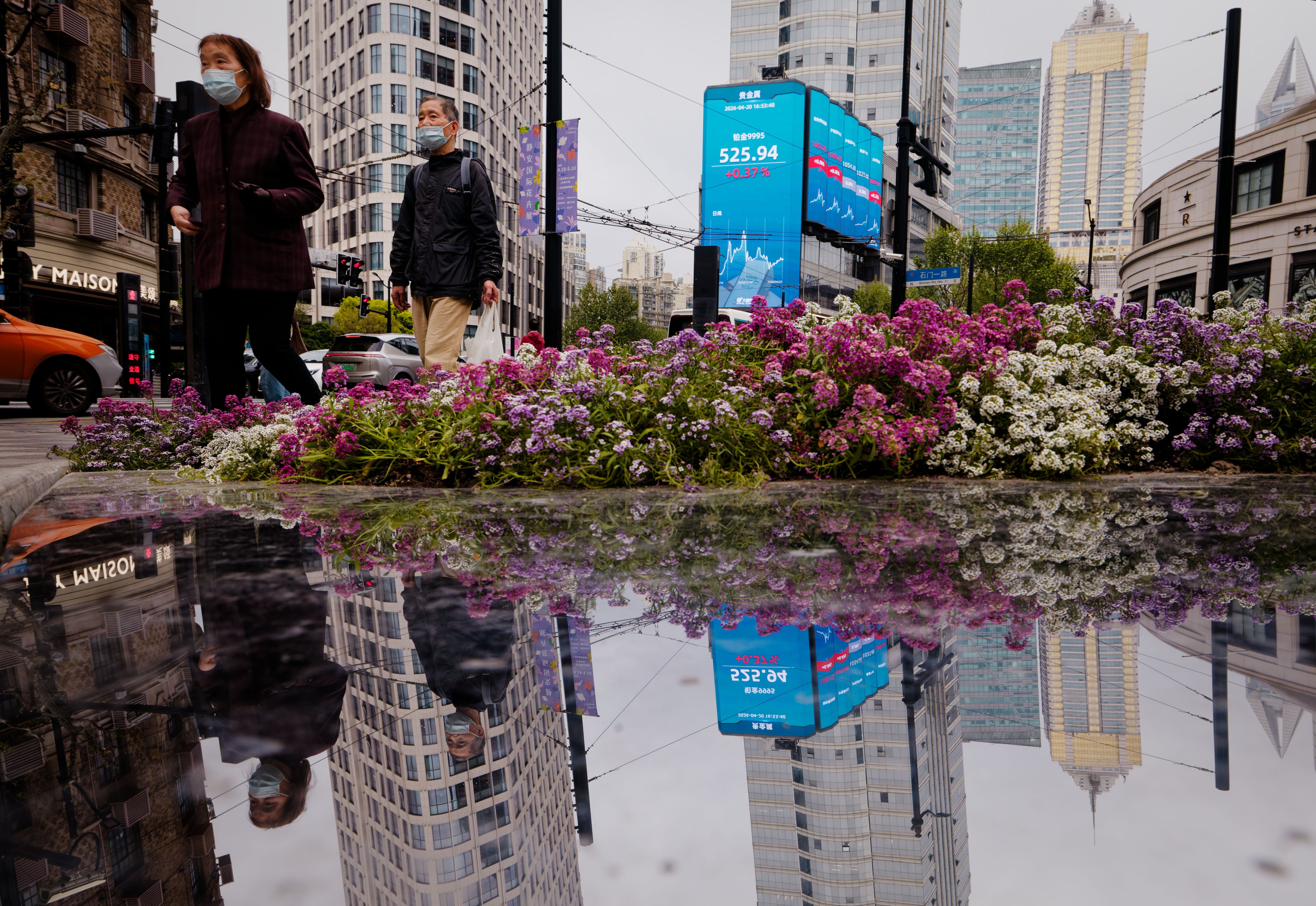 People walk near a screen showing stock exchange and economic data in Shanghai on April 20, 2026. Photo: EPA