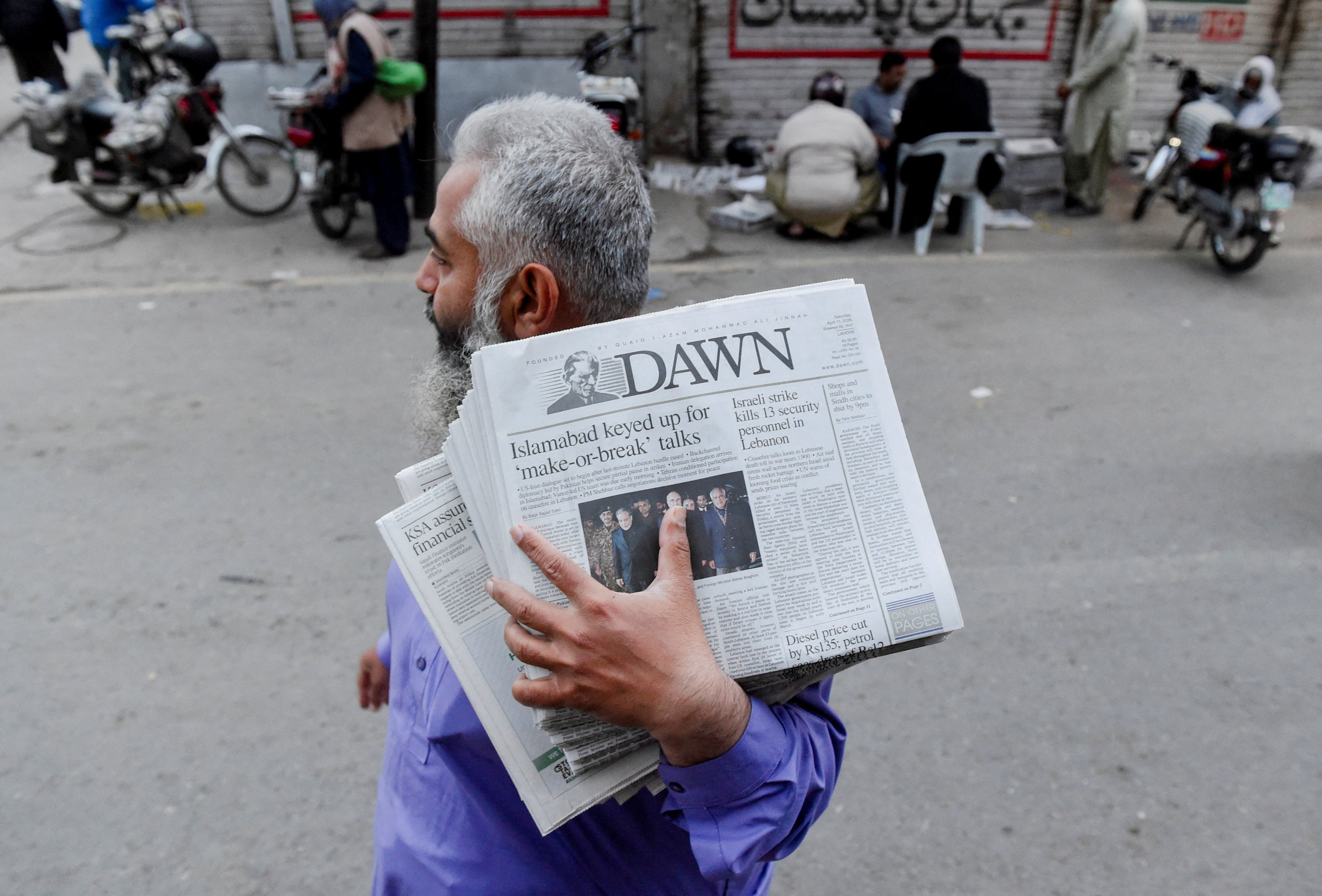 A man carrying a bundle of newspapers with a headline that reads, “Islamabad keyed up for ‘make-or-break’ talks”, walks along a street in Lahore, Pakistan. Photo: Reuters