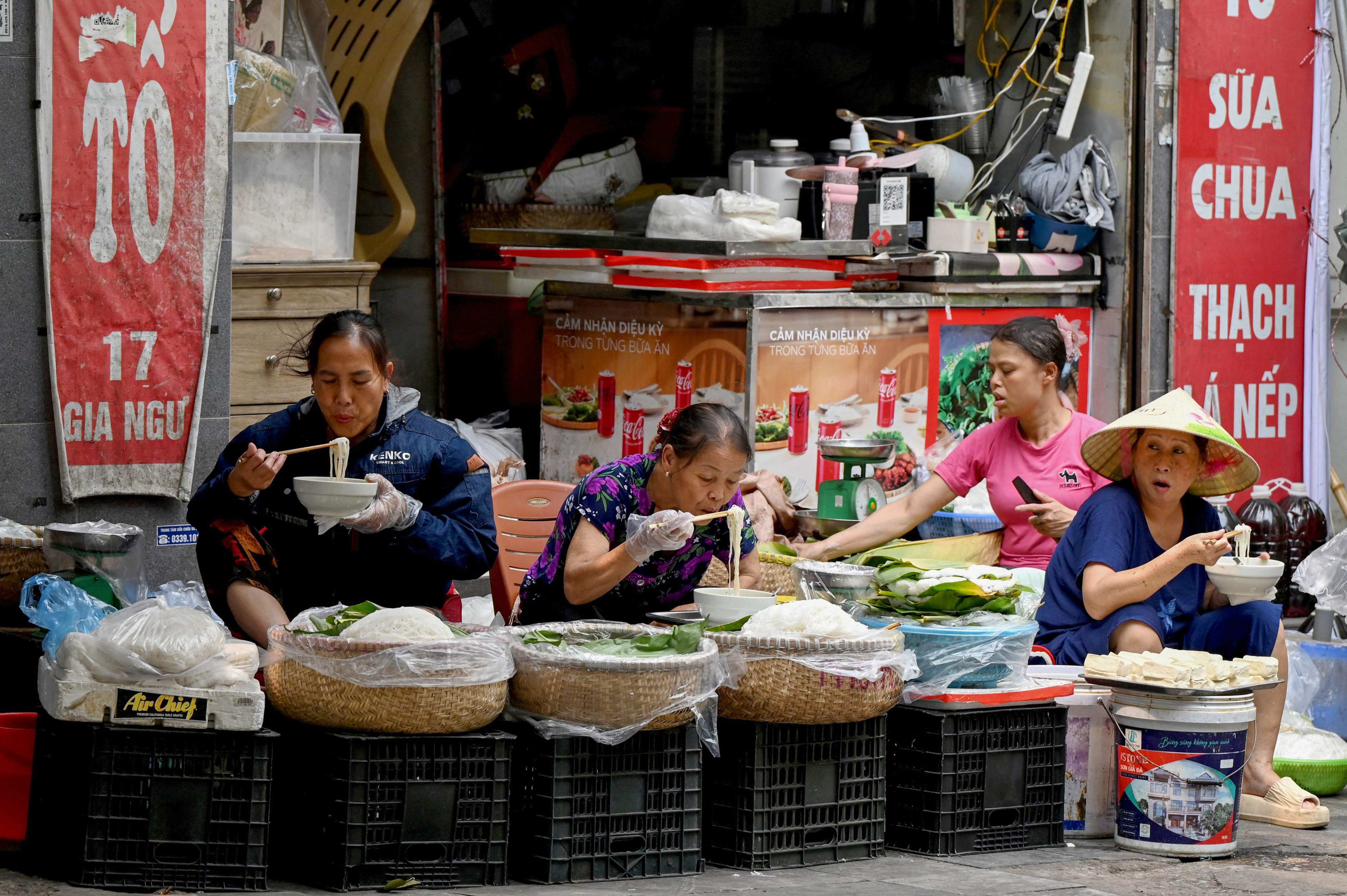 Women sit and eat rice noodles on the sidewalk in Hanoi, Vietnam, on April 14. Photo: AFP