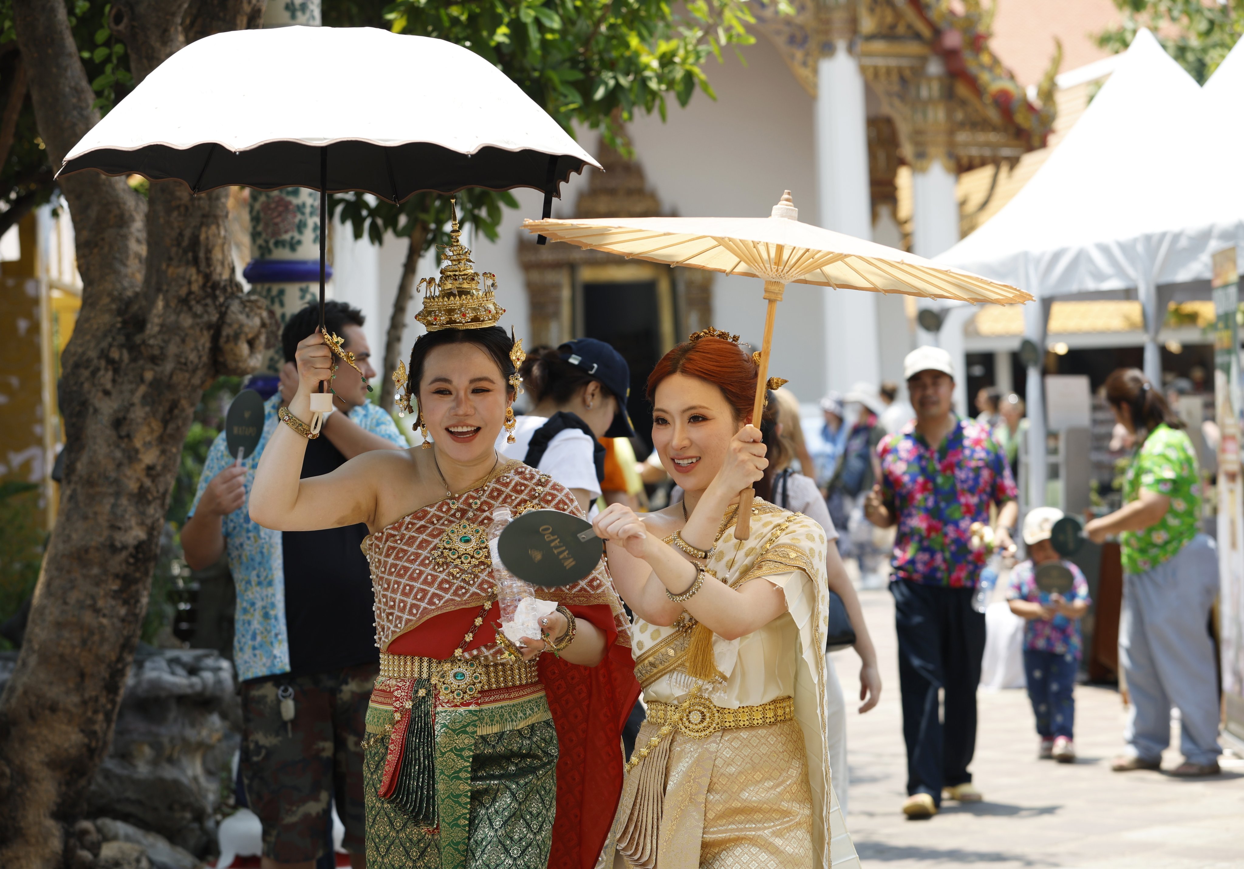 Chinese tourists wearing traditional Thai costumes shield themselves from the sun at Wat Pho, the Temple of the Reclining Buddha, in Bangkok on April 14. Photo: EPA