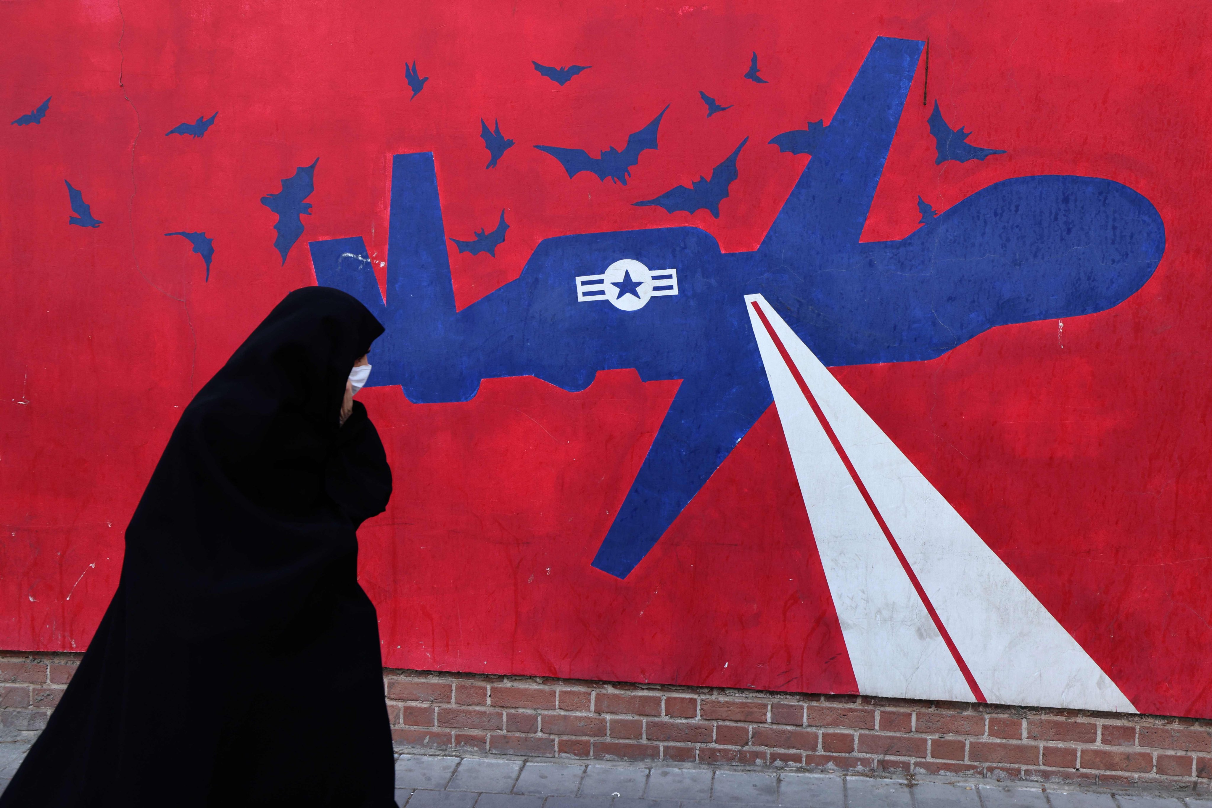 A woman walks past a mural depicting a US drone painted on the outer walls of the former US embassy in Tehran. Photo: AFP