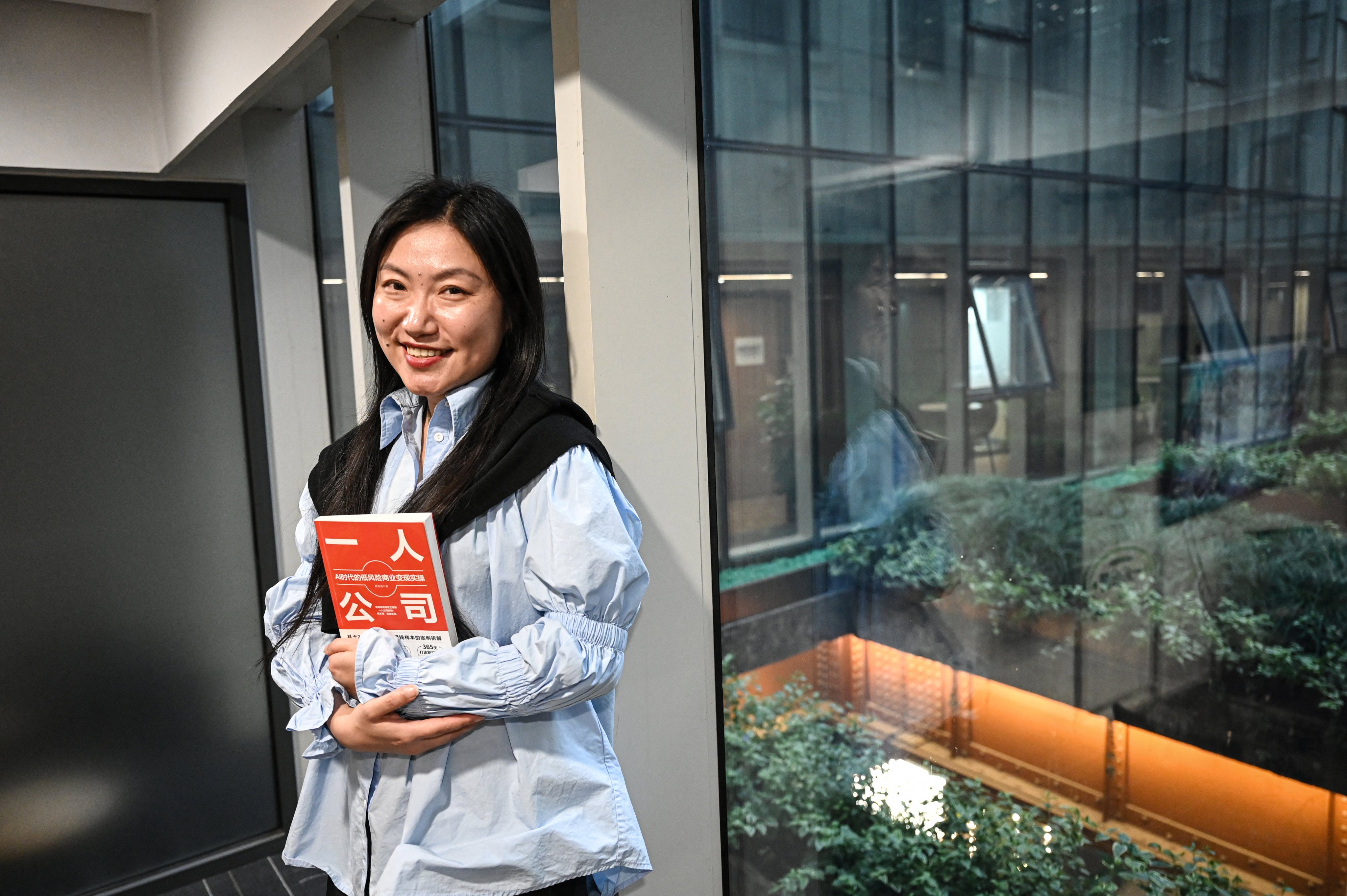 The photo taken on April 12, 2026 shows founder of SoloNest Karen Dai posing for a portrait photo with her new book “One Person Company” at a conference room in Shanghai. Young Chinese, many who fear age discrimination in their workplace after turning 35, are increasingly starting “one-person companies” that have artificial intelligence do most of the work. (Photo by Jade GAO / AFP) / TO GO WITH AFP STORY: China-AI-technology-science-employment, FOCUS by Mary YANG