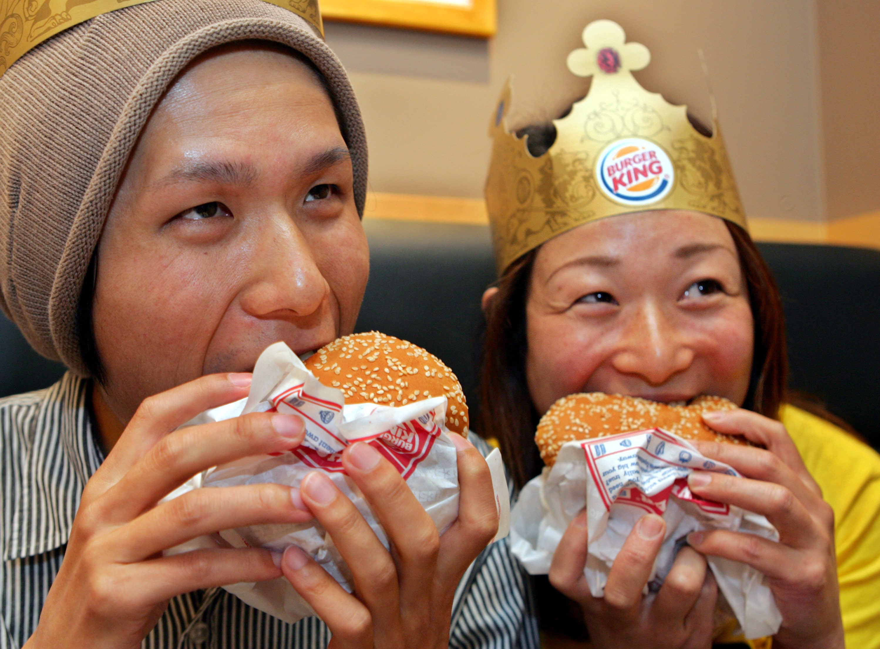 Two customers bite Burger King’s Whopper hamburgers after the chain’s first Tokyo store officially opened in Shinjuku, Tokyo, in 2007. Photo: AP