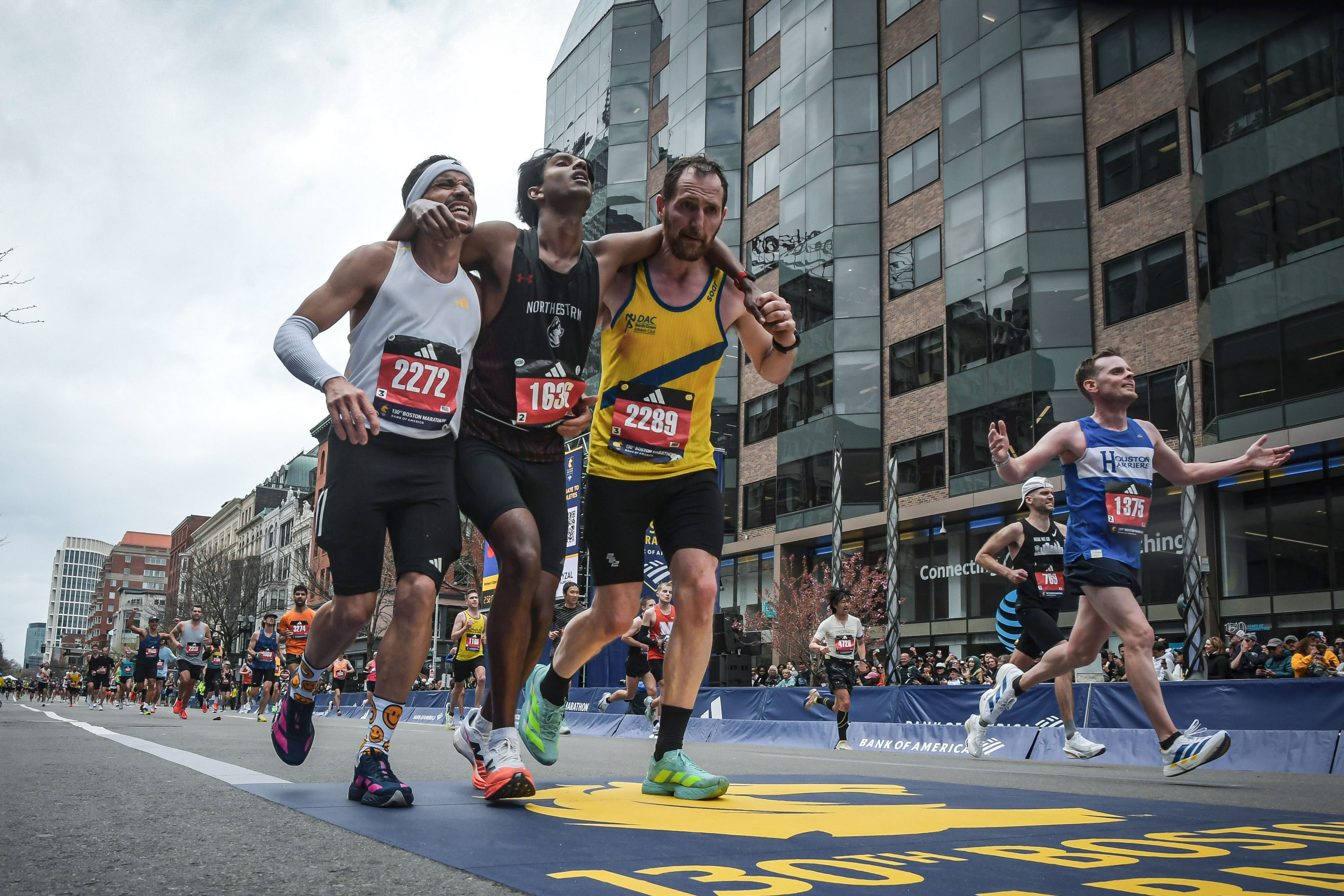 Boston Marathon runners Robson De Oliveira of Brazil (left) and Aaron Beggs of Northern Ireland (right) help Ajay Haridasse across the finish line on Monday. Photo: AP