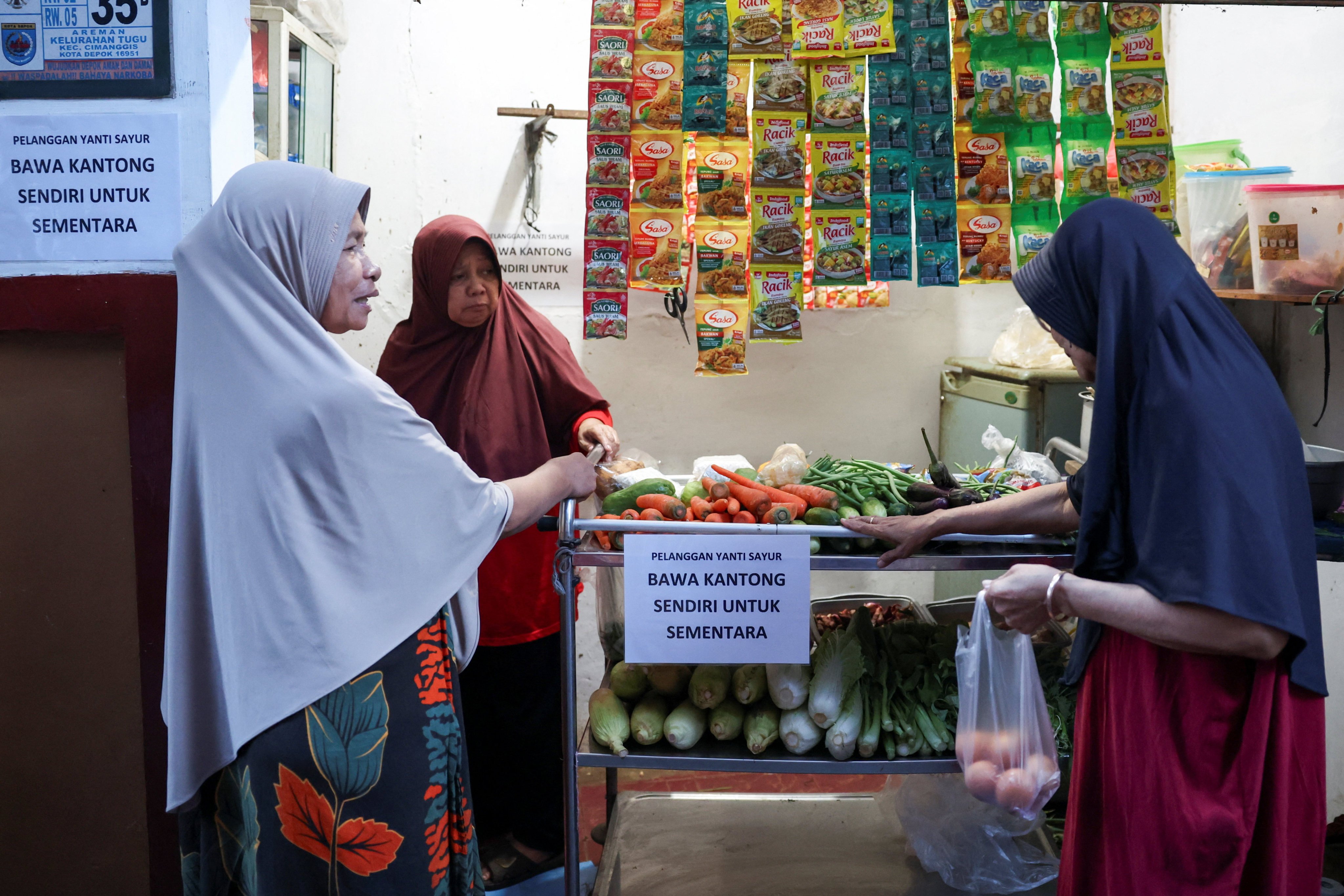 A woman shops for vegetables in Depok, Indonesia, earlier this month near a sign asking customers to bring their own shopping bags. Photo: Reuters