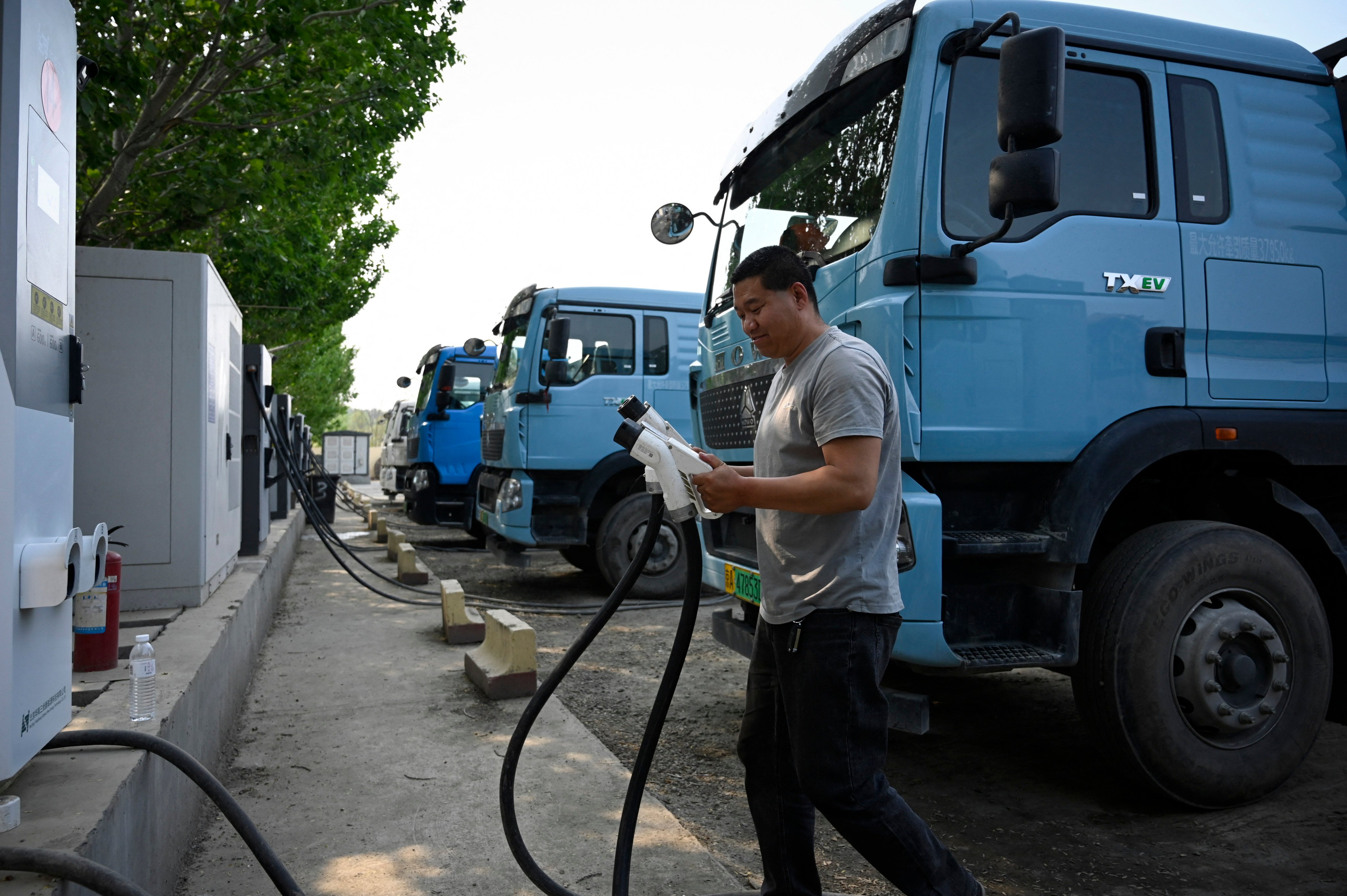 This picture taken on April 23, 2026 shows a driver returning the charging gun after charging his electric truck at a station in Beijing. At a dusty lot an hour outside Beijing, a steady stream of vehicles come and go for a quick battery charge -- just one node in China’s rapidly expanding network of electric trucks. (Photo by WANG Zhao / AFP) / To go with AFP story China-tech-logistics-auto-show, FOCUS by Peter CATTERALL