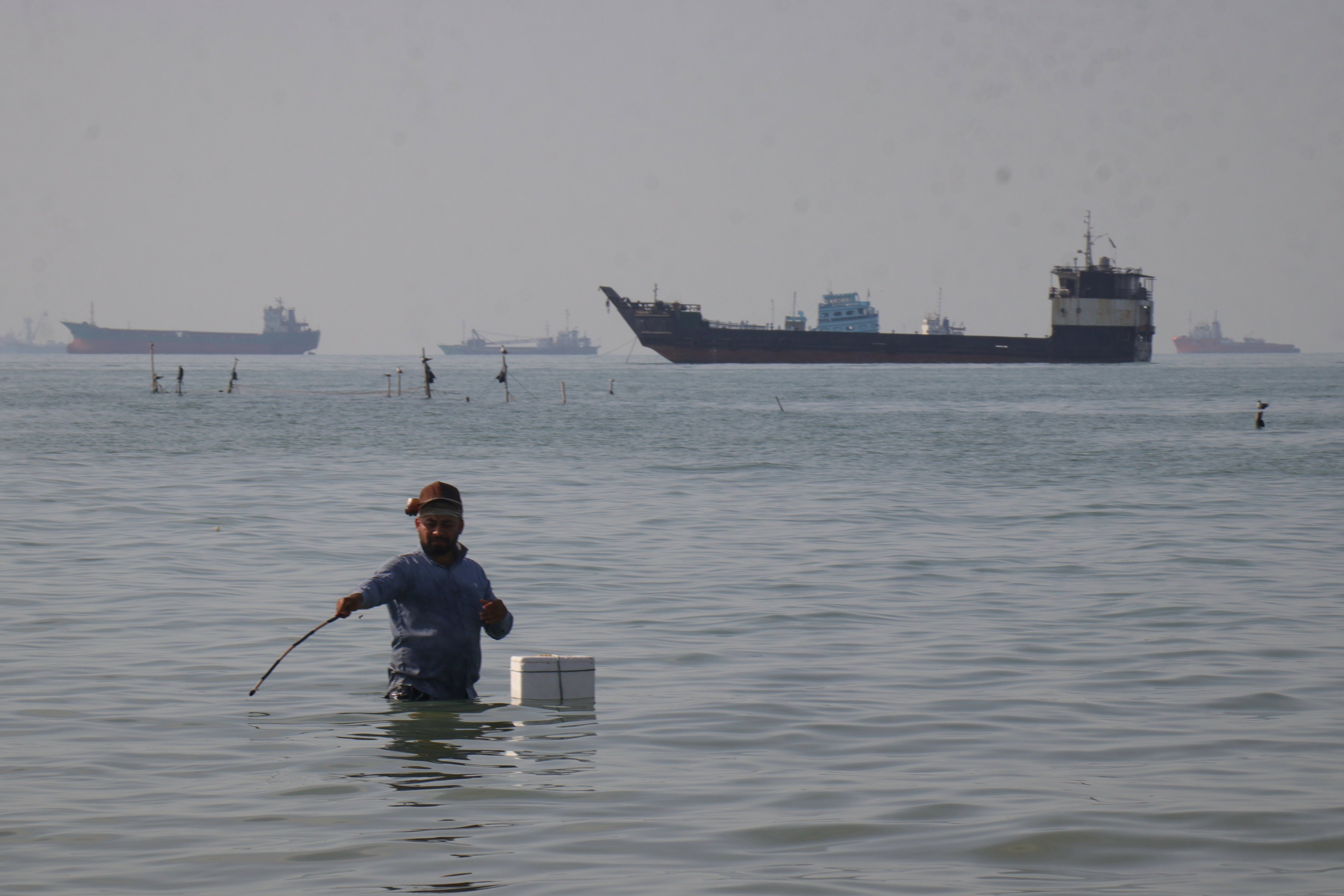 A man stands in the water as ships line the horizon in the Strait of Hormuz in April. Poto: ISNA via AP