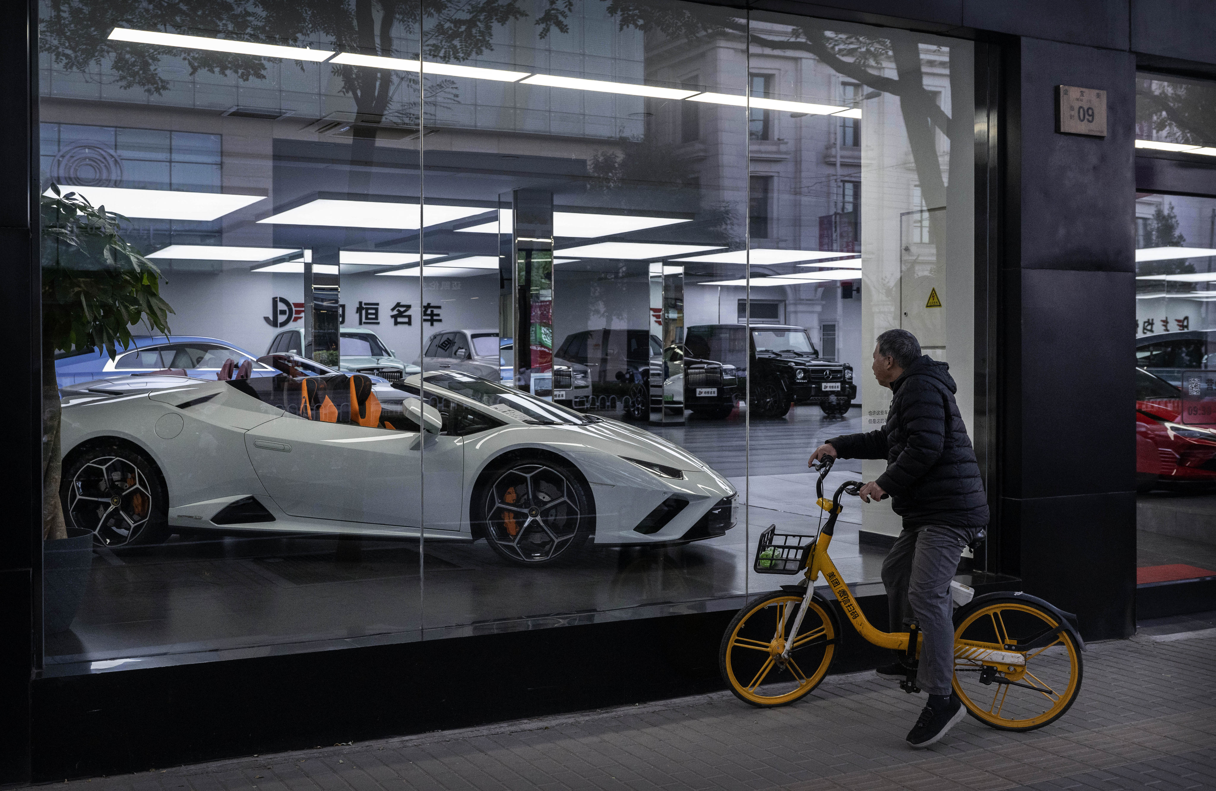A man sits on a shared bike as he looks at a Lamborghini for sale at a luxury car dealership in an upscale commercial area on November 5, 2024, in Beijing. Photo: Getty Images