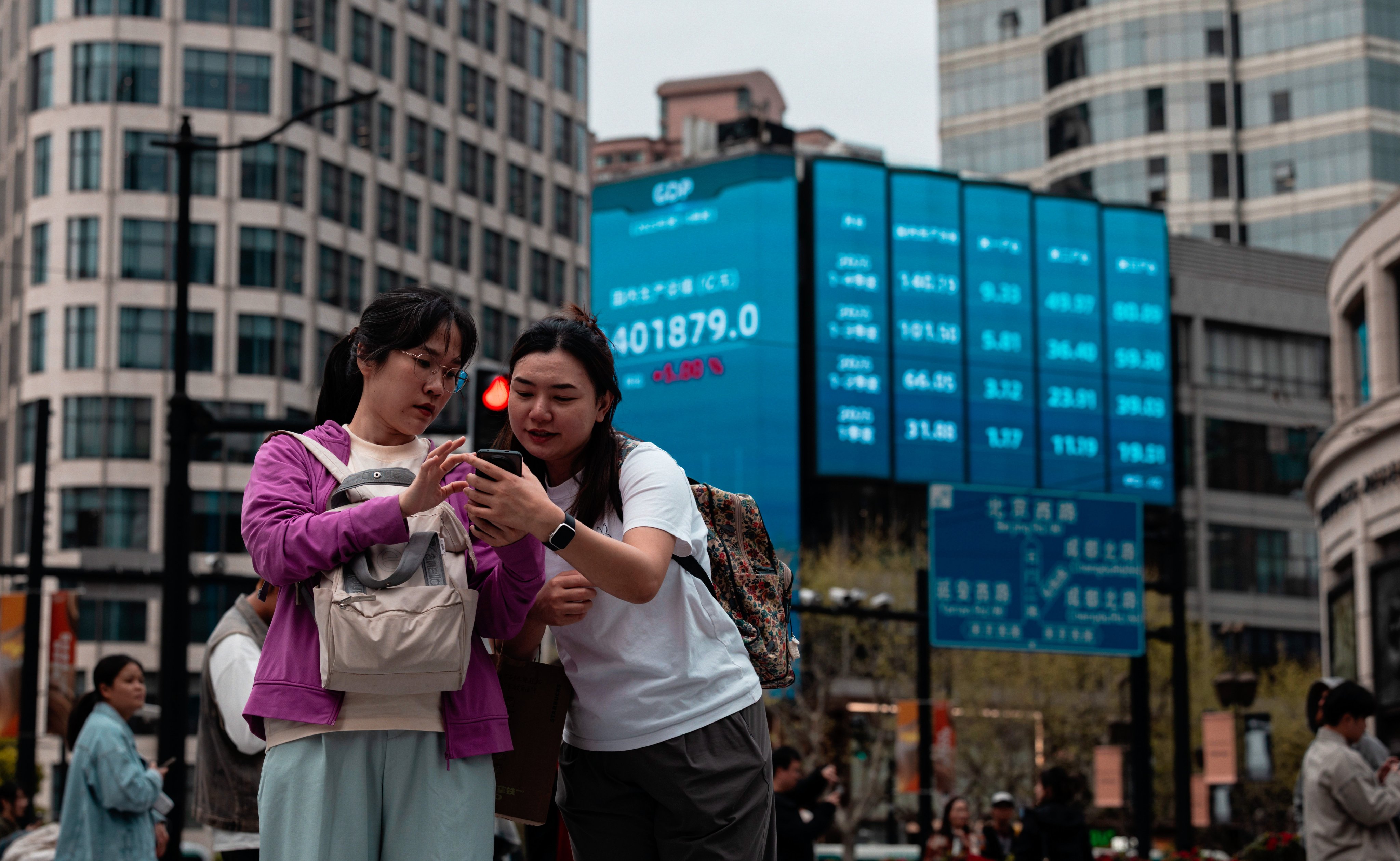 People stand beneath a large screen showing the latest stock prices in Shanghai. Photo: EPA